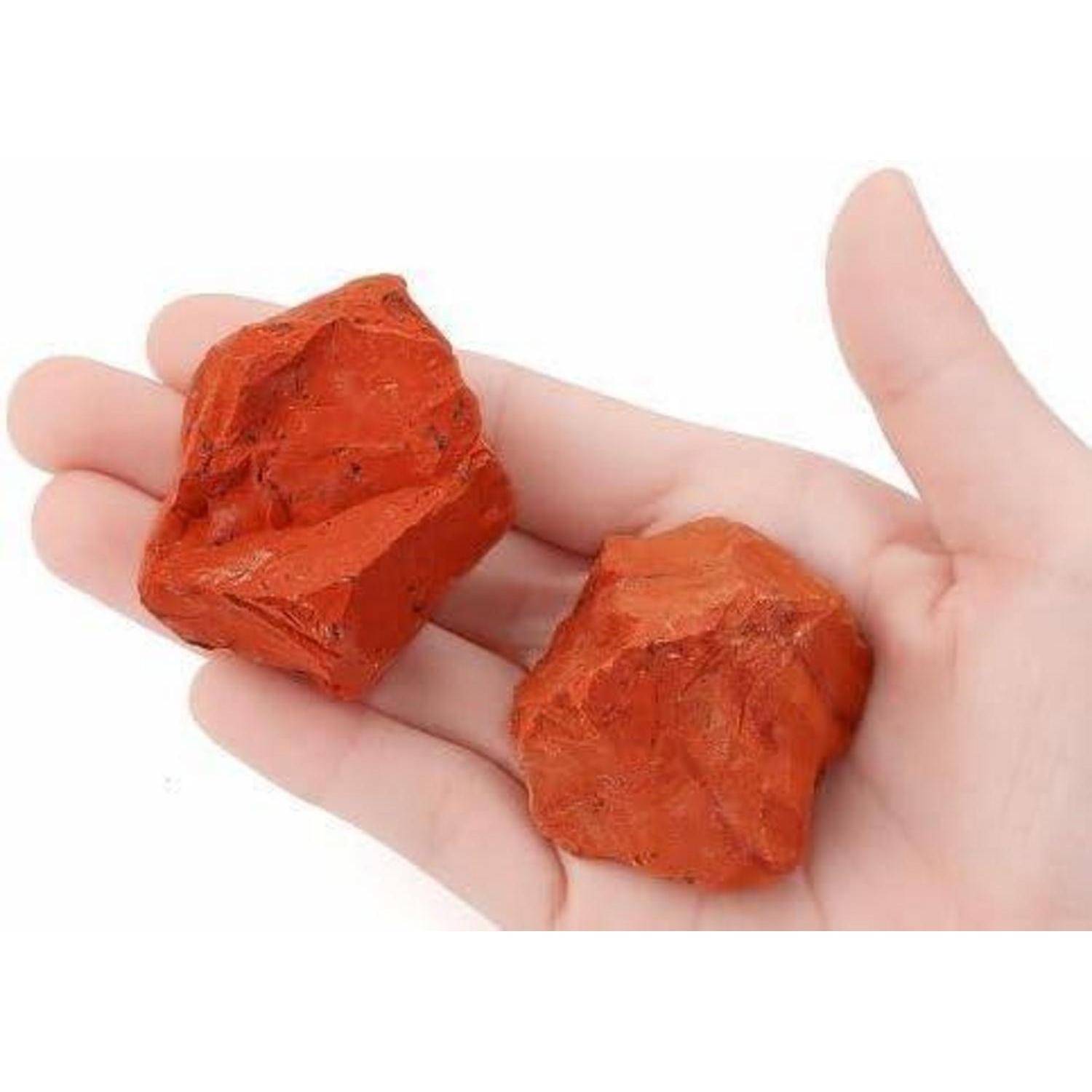 Eine Hand, die zwei Stücke rauer, orangerot-farbener Ockerstein hält. Die Steine haben eine strukturierte Oberfläche und haben etwa die Größe kleiner Gesteinsbrocken.