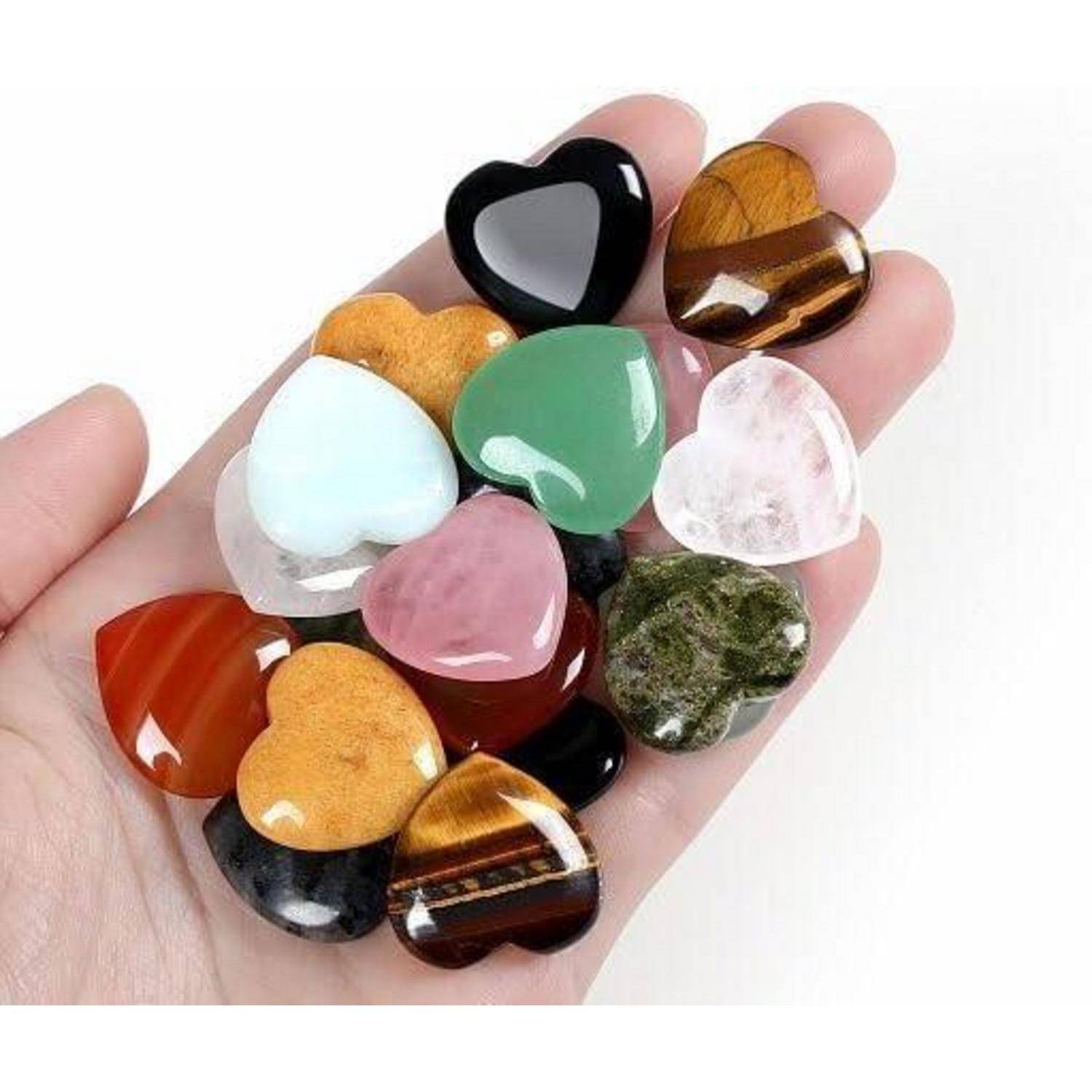 Eine Hand hält verschiedene herzförmige Steine in unterschiedlichen Farben und Mustern, darunter schwarz, braun, grün und rosa.