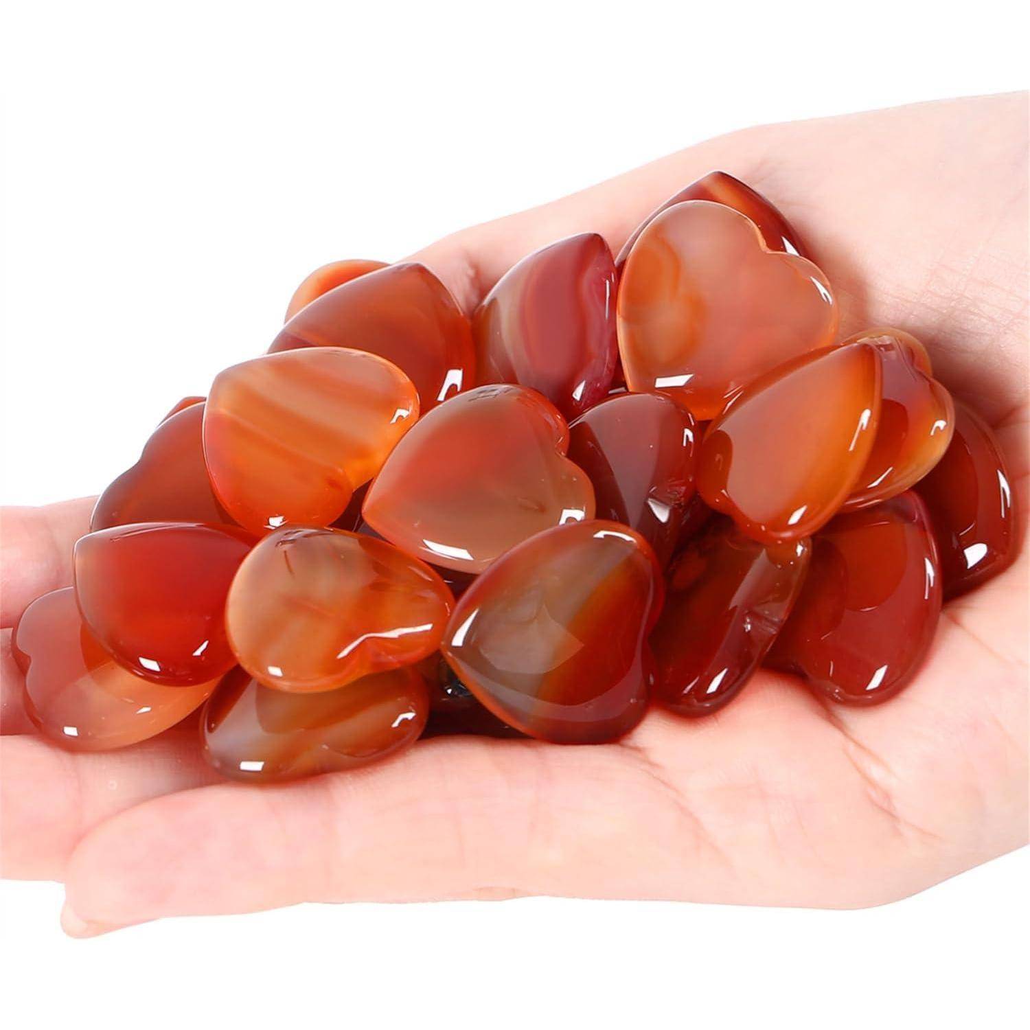 Eine Hand, die glatte, polierte Achatsteine in Rot und Orange hält, die das Licht reflektieren und in einem kleinen Haufen angeordnet sind.