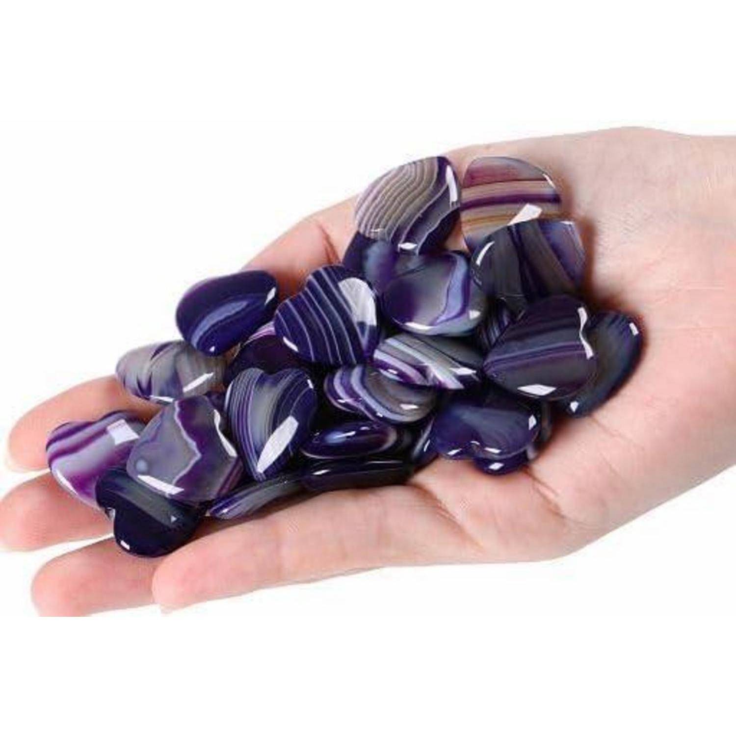 Eine Hand, die mehrere polierte, violette Achatsteine mit weißen Streifen hält.