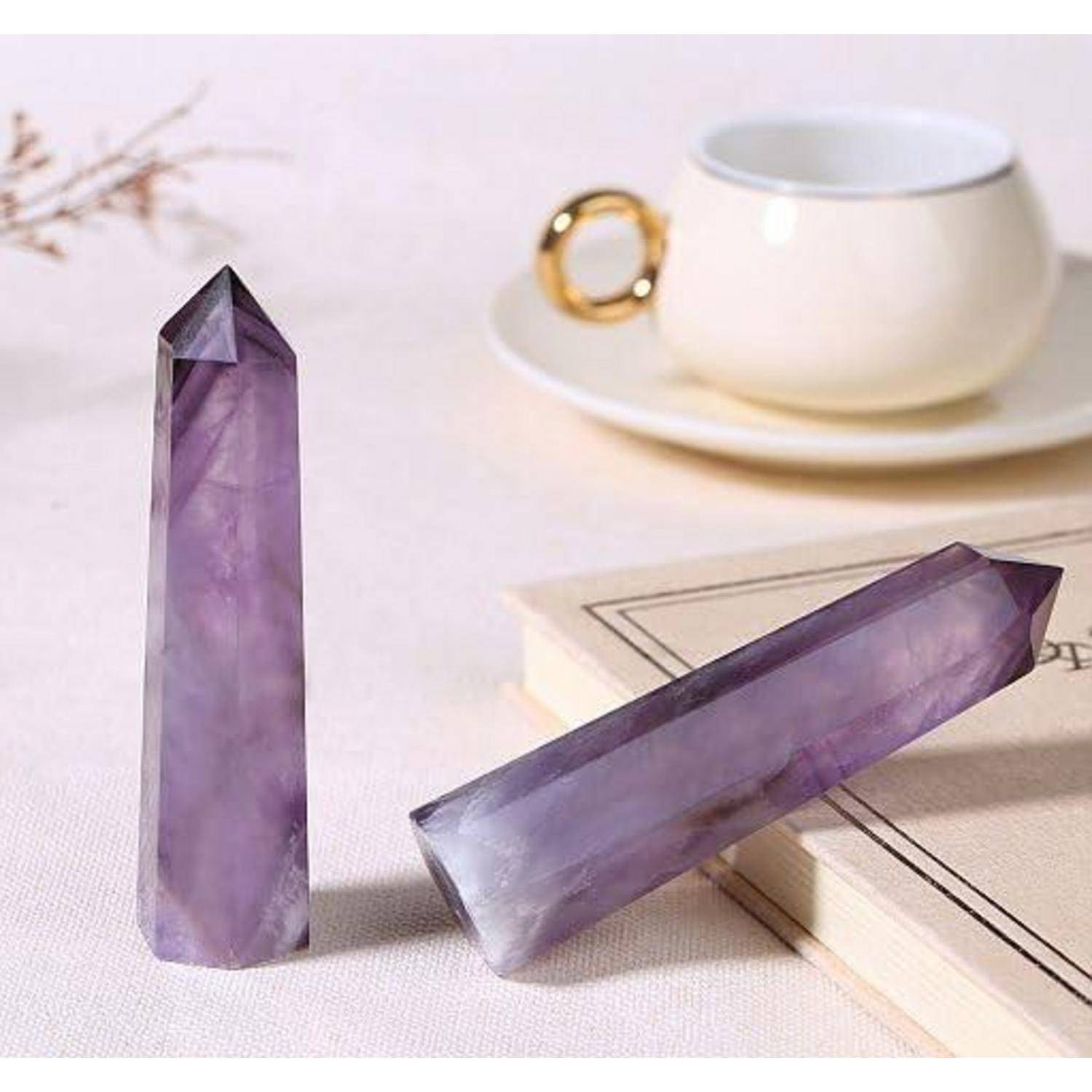 Zwei Amethystkristalle, einer vertikal und einer horizontal, auf einem Buch neben einer weißen Tasse mit goldenem Henkel, auf einer hellen Oberfläche platziert.