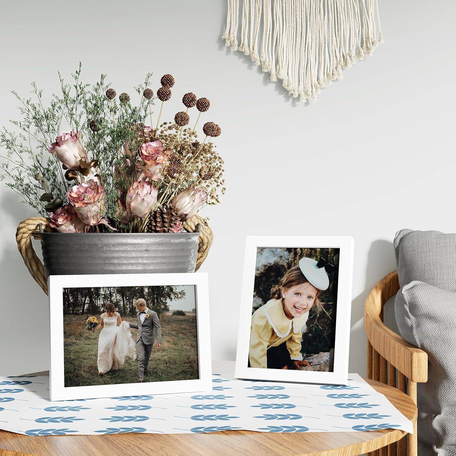 Ein Tisch mit gerahmten Fotos: eines von einem Brautpaar im Freien, ein anderes von einem lächelnden Kind. Eine Blumenarrangement und ein Wandbehang befinden sich im Hintergrund.