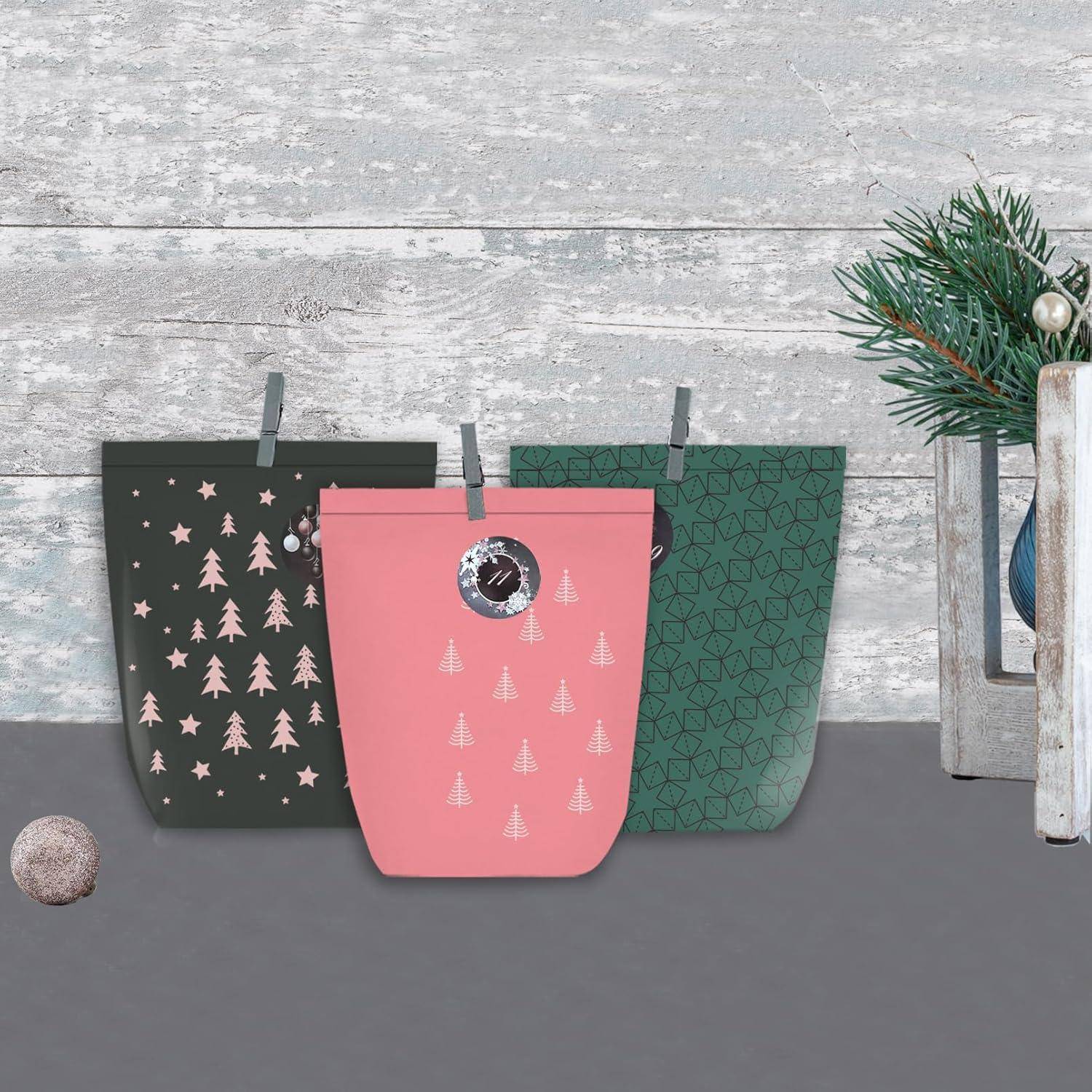 Drei Geschenktüten mit weihnachtlichen Motiven in Rosa, Grün und Schwarz sind auf einer grauen Oberfläche vor einem festlichen Hintergrund angeordnet.