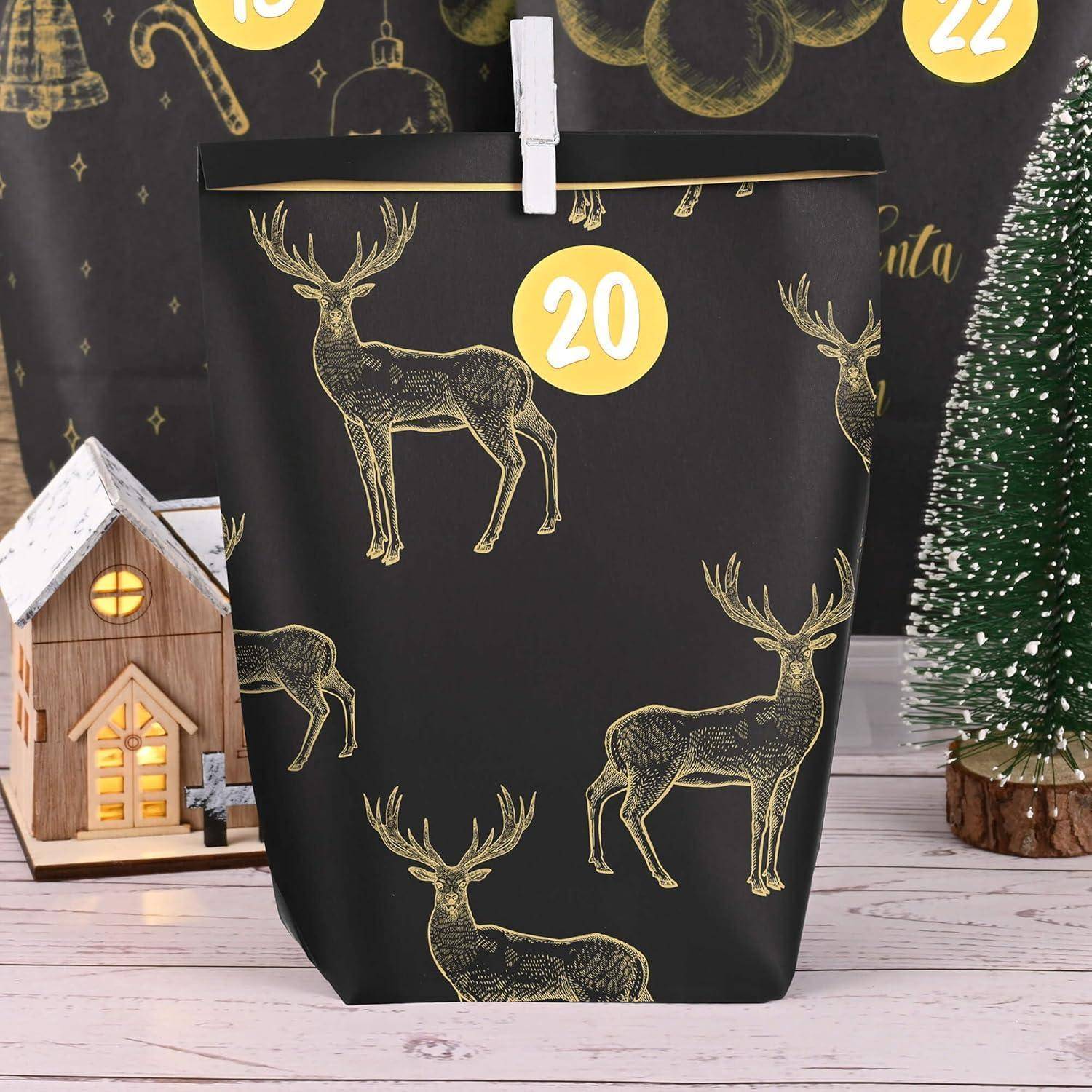 Ein schwarzer Adventskalender mit goldenen Rentieren und einer weißen '20'. Ein kleines Holzhaus und ein Weihnachtsbaum in der Nähe auf einer Holzoberfläche.
