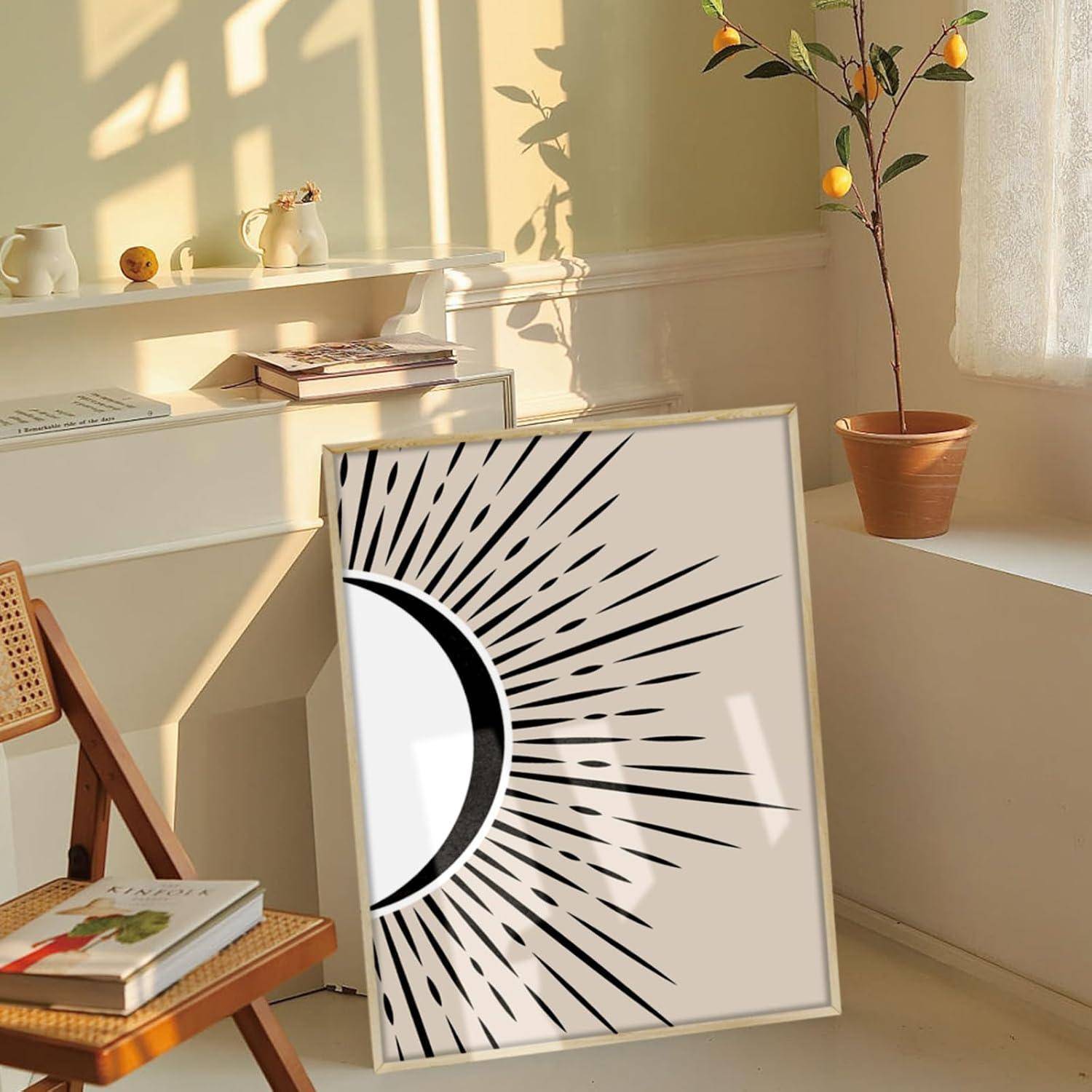 Ein gerahmter Druck mit einem Sonnenstrahlen-Design, das schwarze Strahlen zeigt, sitzt auf einem Stuhl in einem warm beleuchteten Raum, mit Büchern und Topfpflanzen auf Regalen.