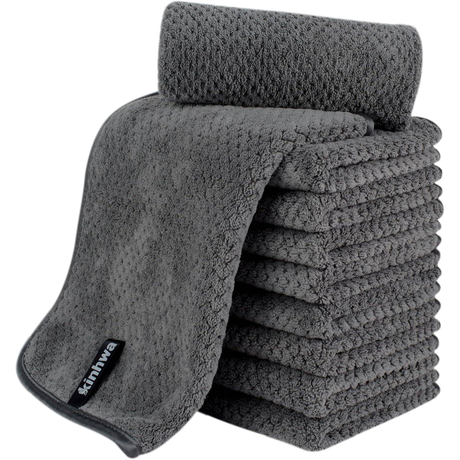 Ein Stapel von zehn grauen gestrickten Handtüchern mit einem strukturierten Muster; ein Handtuch ist oben teilweise ausgefaltet, das schwarze Markenlabel ist in der Ecke sichtbar.