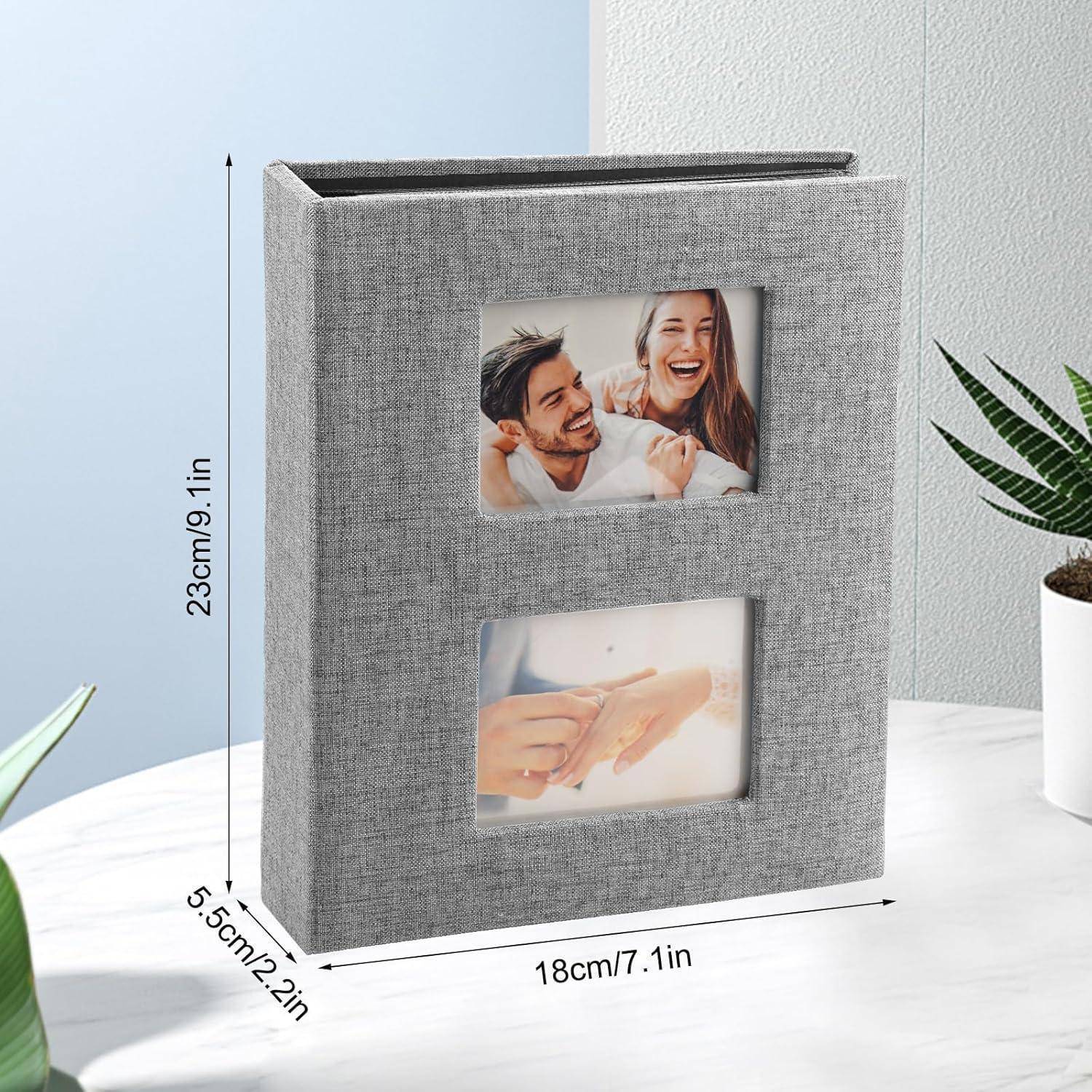 Ein grauer Stofffotoalbum mit zwei Bildschlitzen auf dem Einband: Oben ein lächelndes Paar, unten Hände mit Ringen. Die Abmessungen des Albums betragen 23 cm x 18 cm x 5,5 cm.