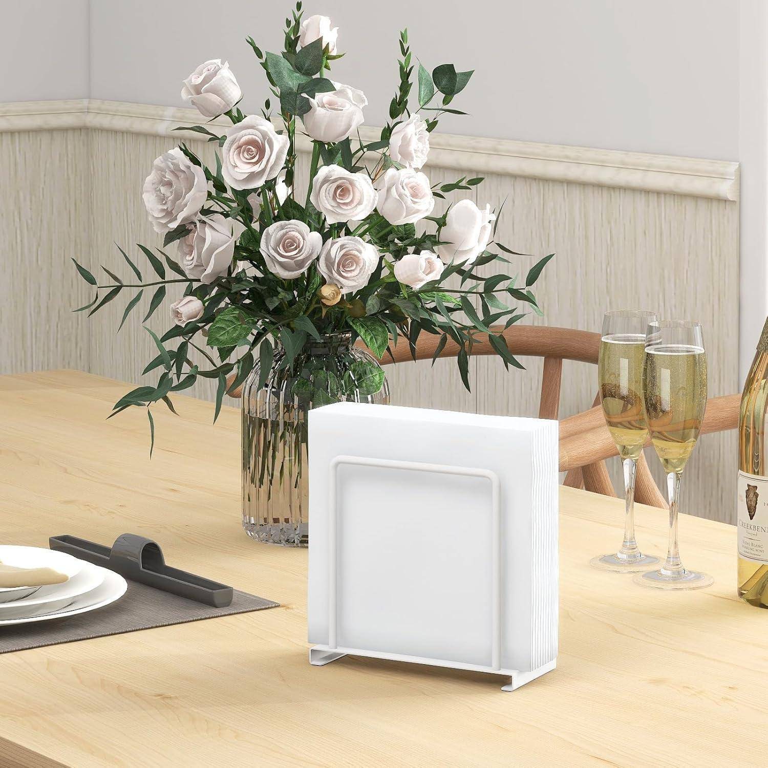 Ein Esstisch, der mit einem Blumengesteck, Weingläsern und Küchenutensilien gedeckt ist; Eckregal und Weinflasche im Hintergrund.