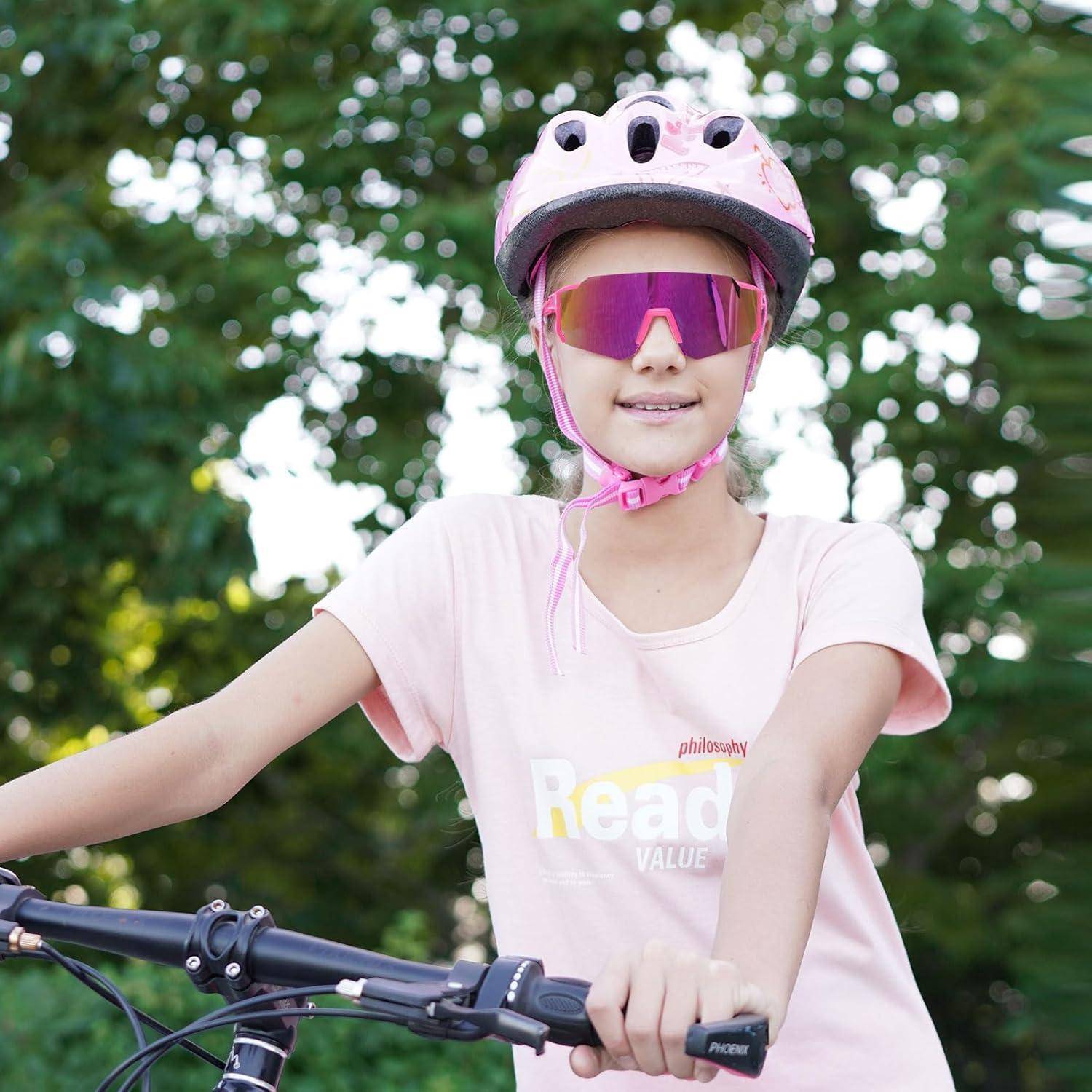 Ein Kind mit einem rosa Helm und Brille fährt Fahrrad in einem Park und trägt ein rosa T-Shirt mit der Aufschrift ‚Ready'.