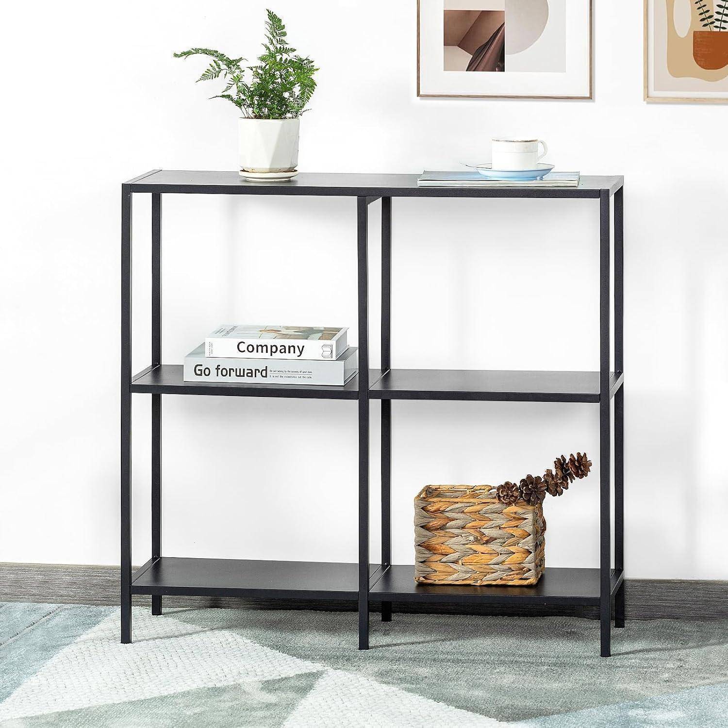 Ein minimalistisches schwarzes Metallregal mit drei Ebenen, das eine Pflanze, ein kleines gerahmtes Bild, ein Buch mit dem Titel ‚Geh vorwärts' und einen geflochtenen Korb trägt.