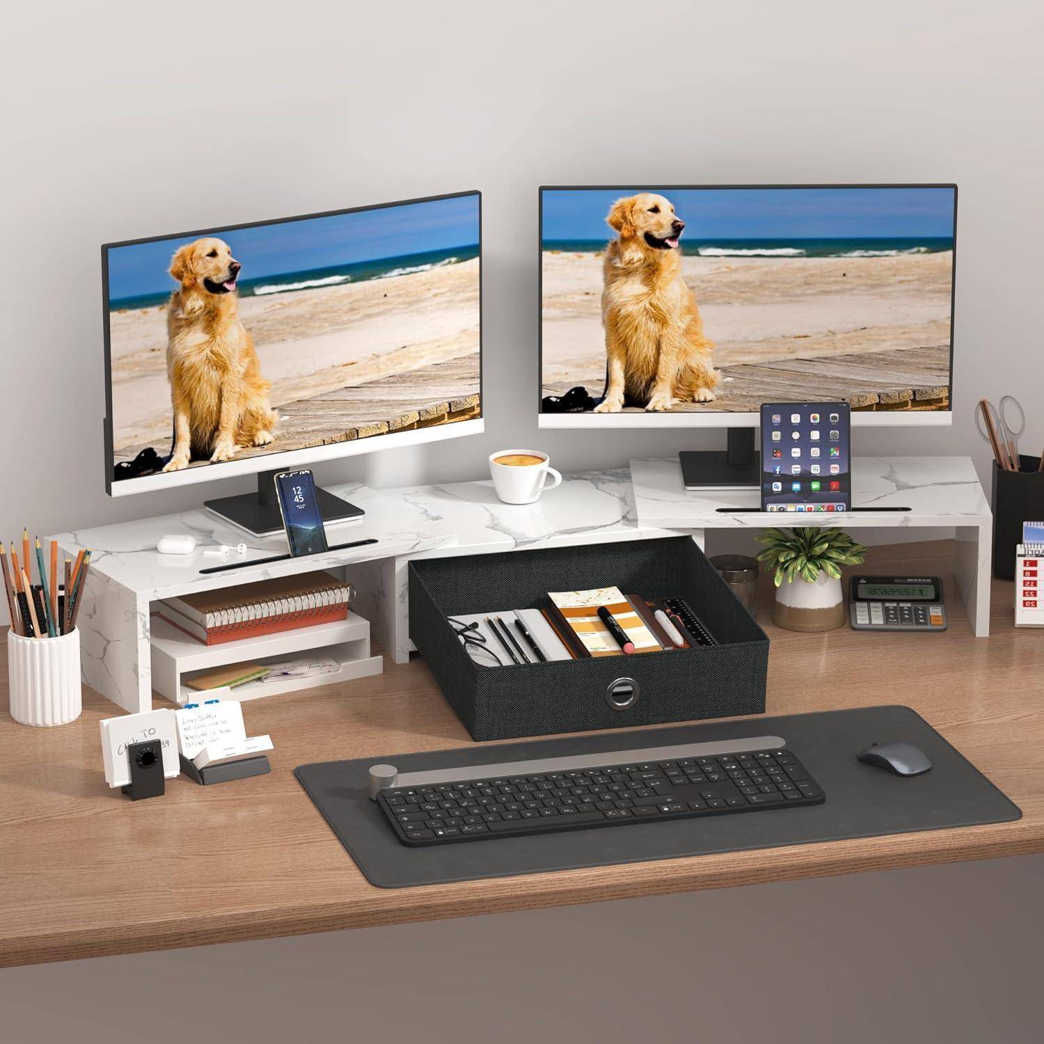 Ein aufgeräumter Schreibtisch mit zwei Monitoren, die Hundebilder zeigen, einer Tastatur, einer Maus, einem Telefon auf einem Ständer, einem Tablet und ordentlich arrangierten Büromaterialien.