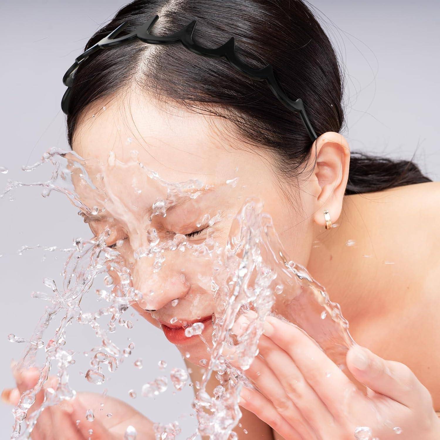 Eine Frau mit einem Stirnband spritzt sich Wasser ins Gesicht, was auf Hautpflege oder einen erfrischenden Moment hindeutet.