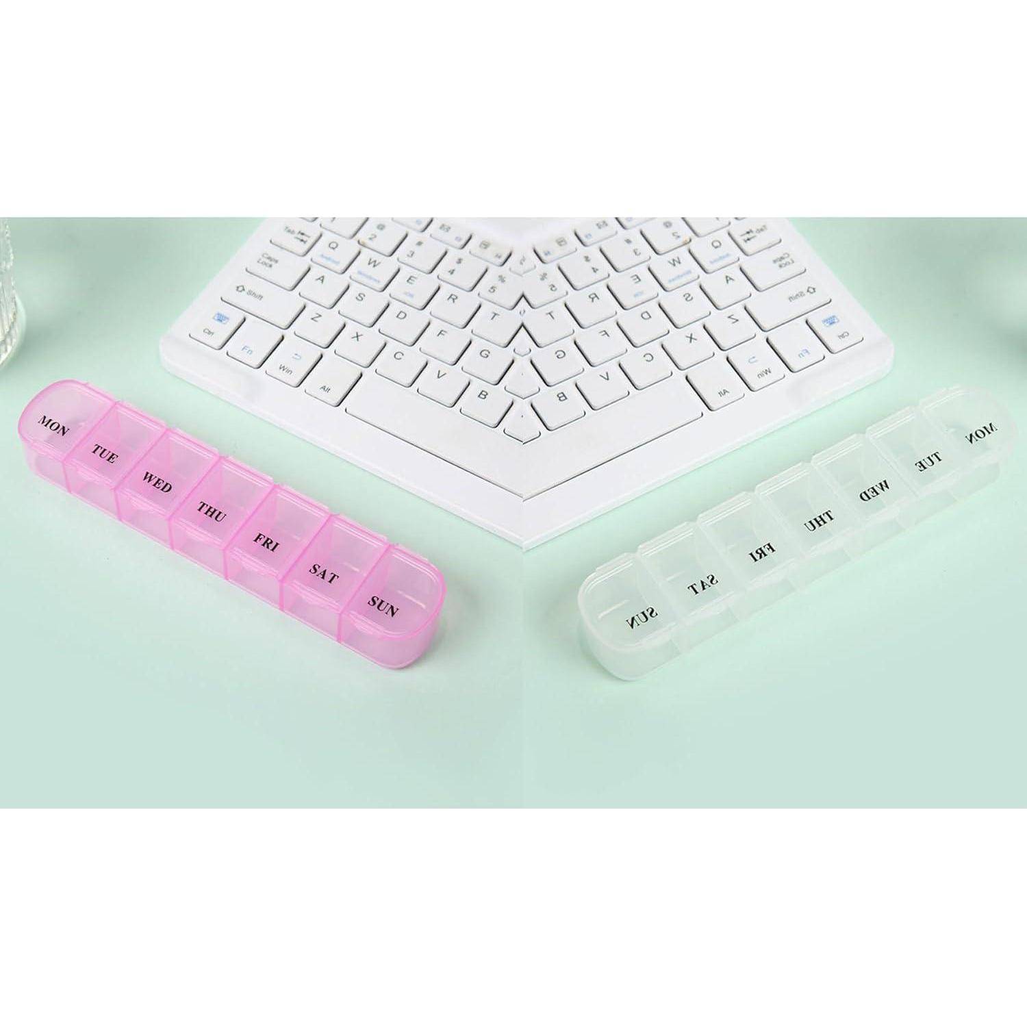 Zwei wöchentliche Pillendosen mit Tageskennzeichnung, eine in Rosa und eine in Weiß, die neben einer Computertastatur auf einer hellgrünen Oberfläche platziert sind.