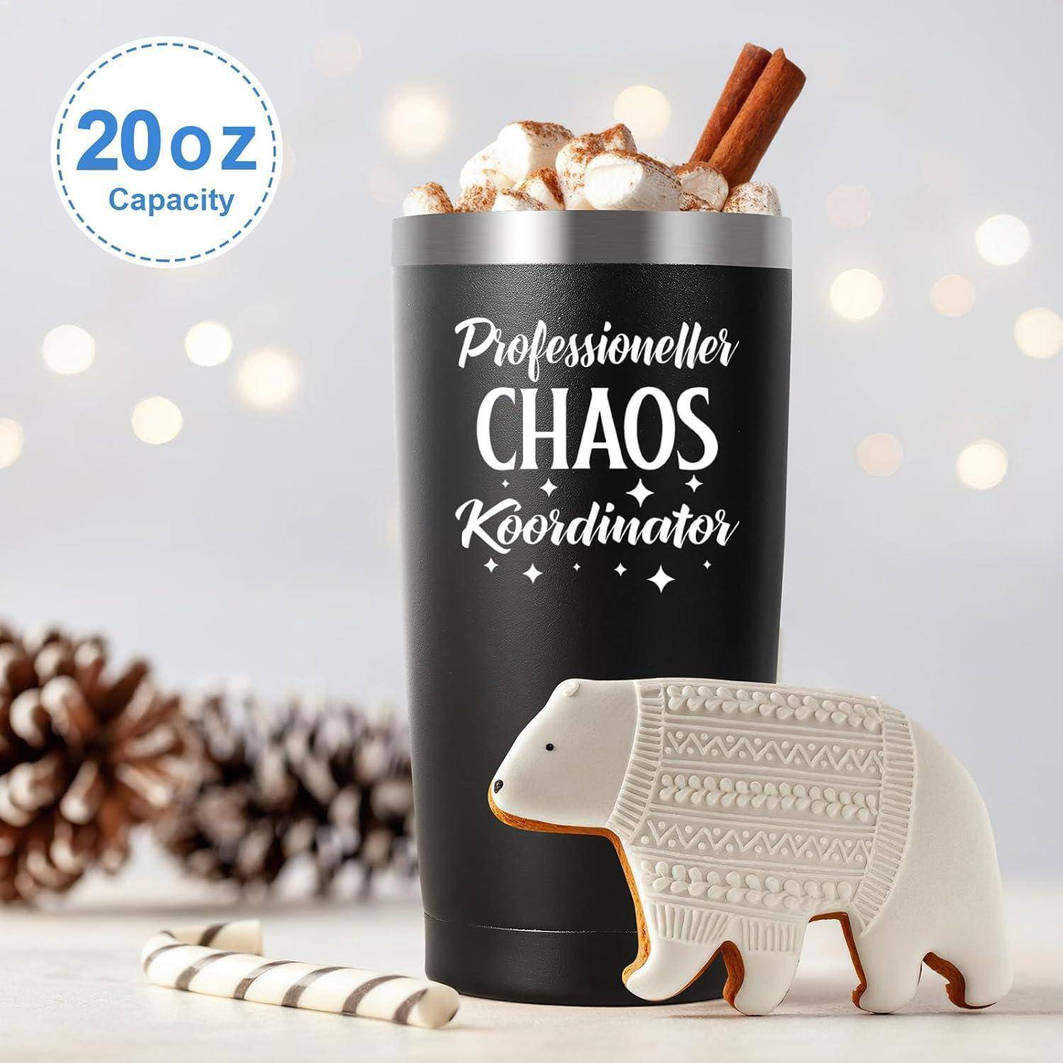 Eine schwarze Tasse mit dem Aufdruck 'Professioneller Chaos Koordinator', gefüllt mit Marshmallows und Zimtstangen, neben einem dekorativen Bärchen-Keks.