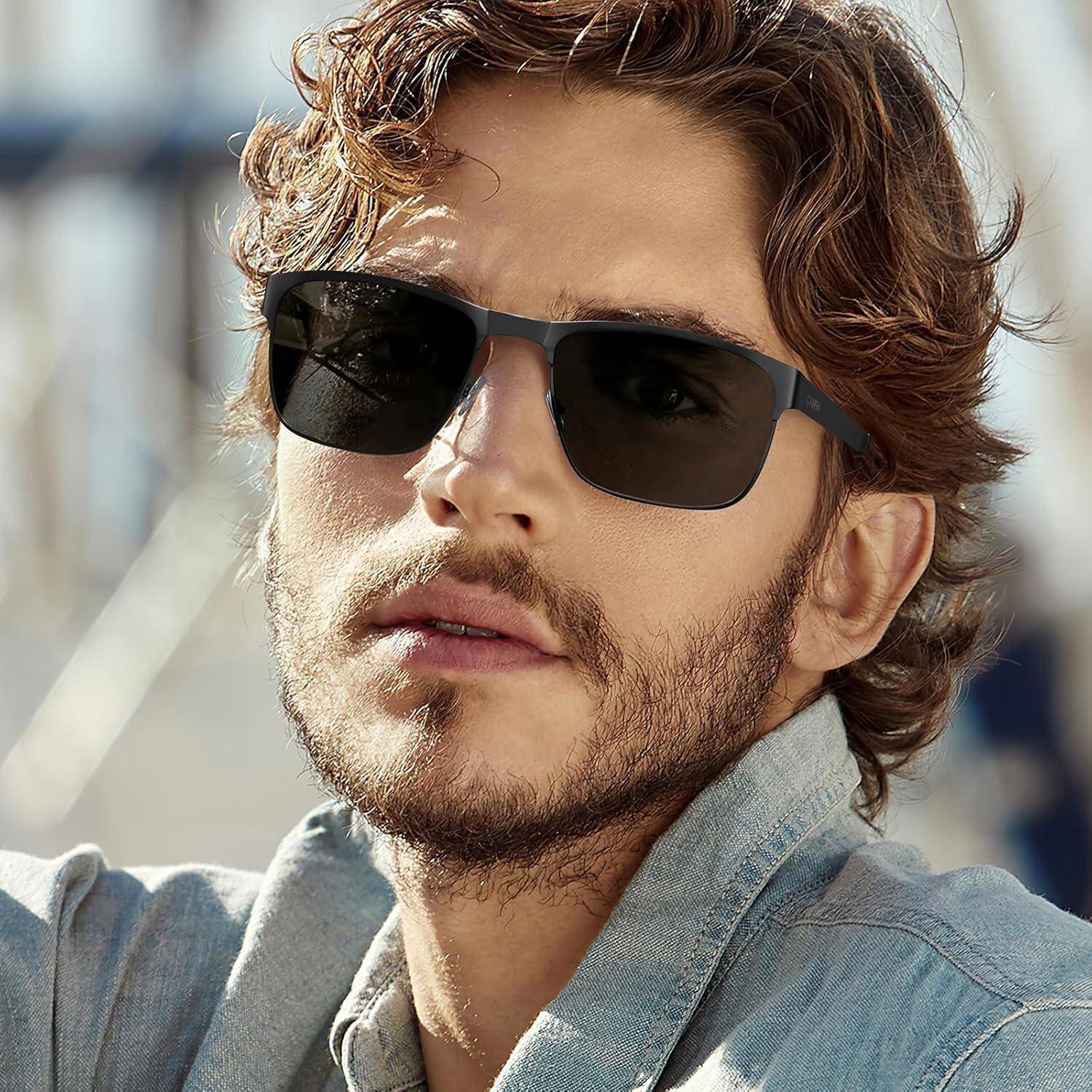 Eine Person mit lockigem Haar trägt eine Sonnenbrille und ein hellblaues Hemd und posiert im Freien.