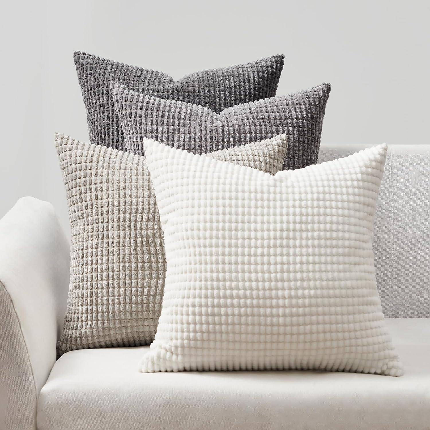 Vier strukturierte Kissen in neutralen Tönen sind auf einem weißen Sofa angeordnet und zeigen einen gemütlichen und eleganten Einrichtungsstil.
