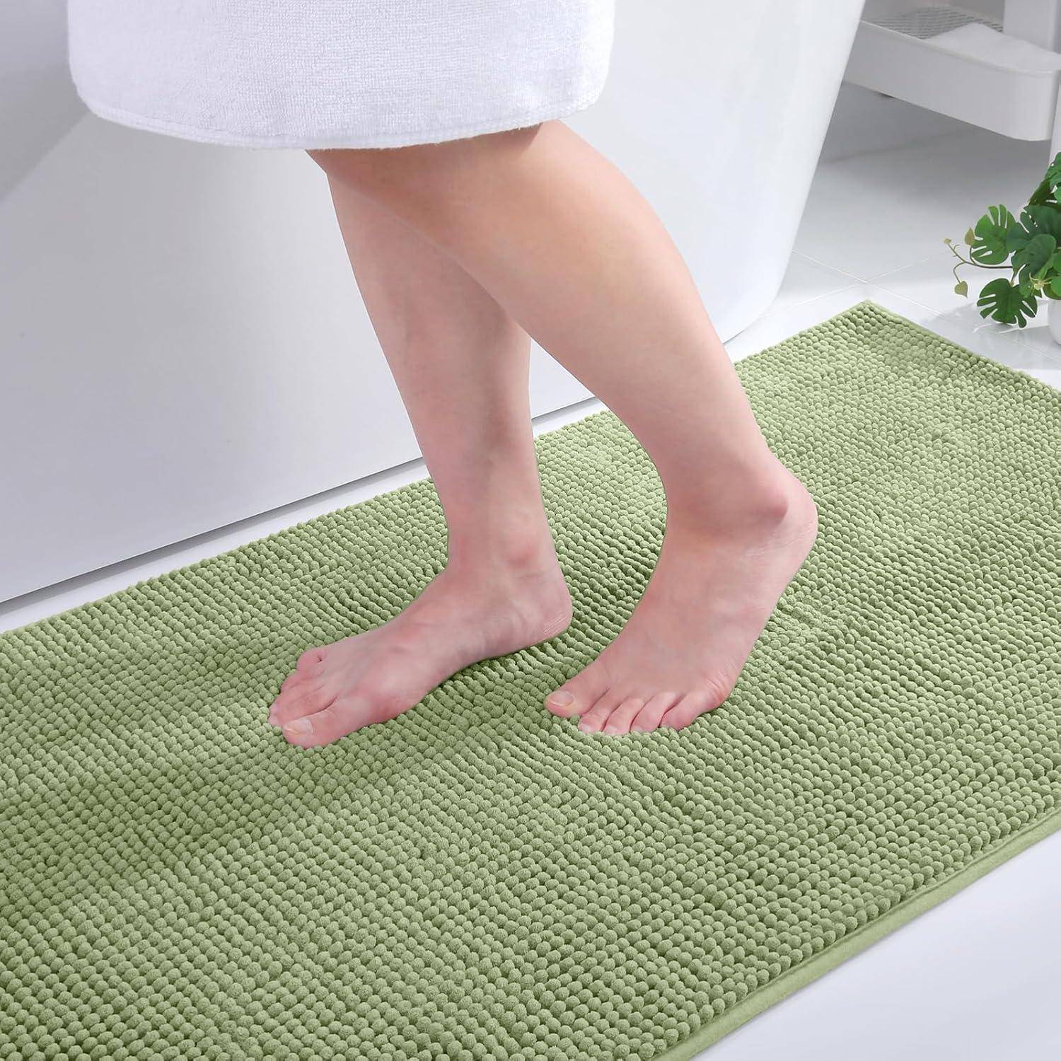 Eine Person steht barfuß auf einer grünen, strukturierten Badematte neben einer weißen Badewanne und unterstreicht dabei Komfort und Weichheit.