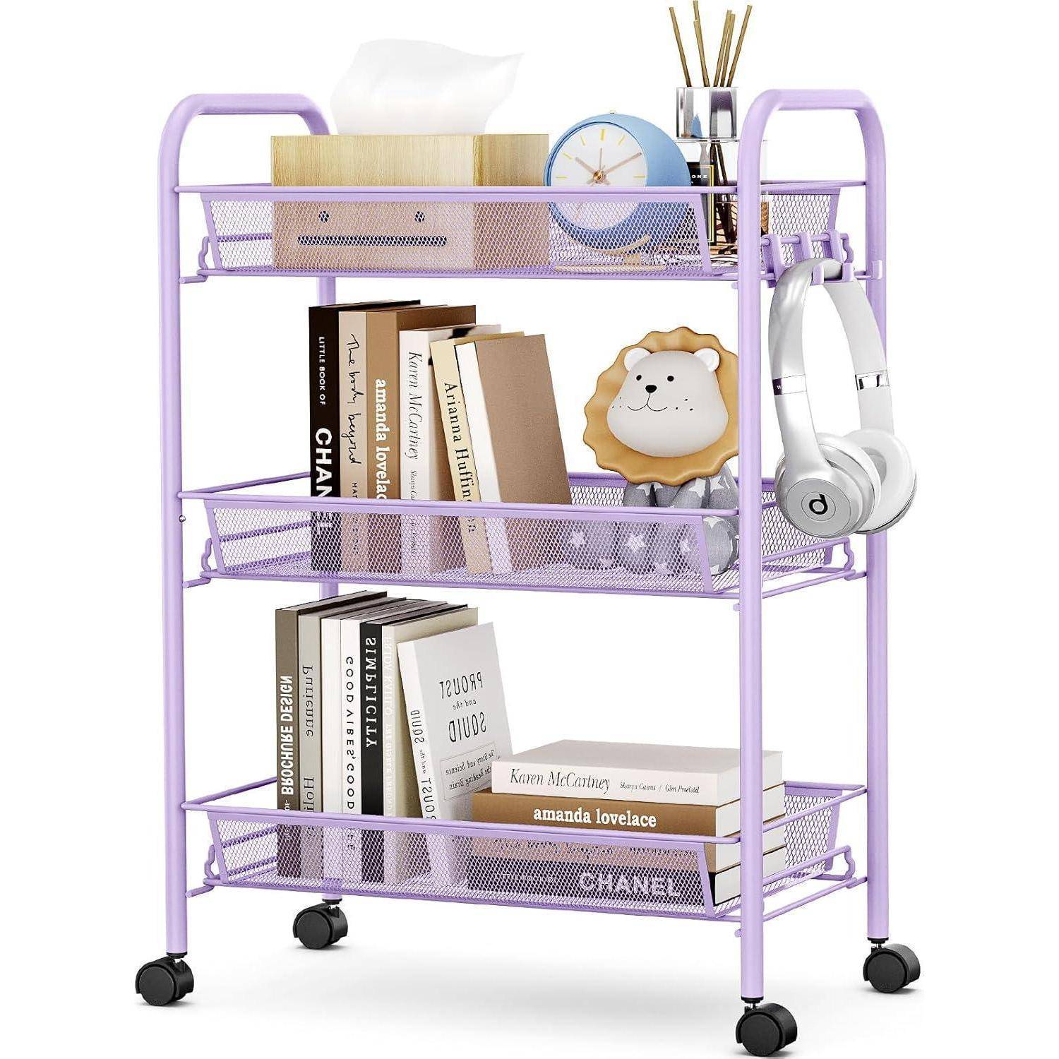 Lila Rollwagen mit drei Ebenen, bestückt mit Büchern, einer Taschentuchbox, einer Uhr, einem Löwen-Ornament und Kopfhörern. Die Gegenstände sind auf jeder Ablage sorgfältig und ordentlich angeordnet.