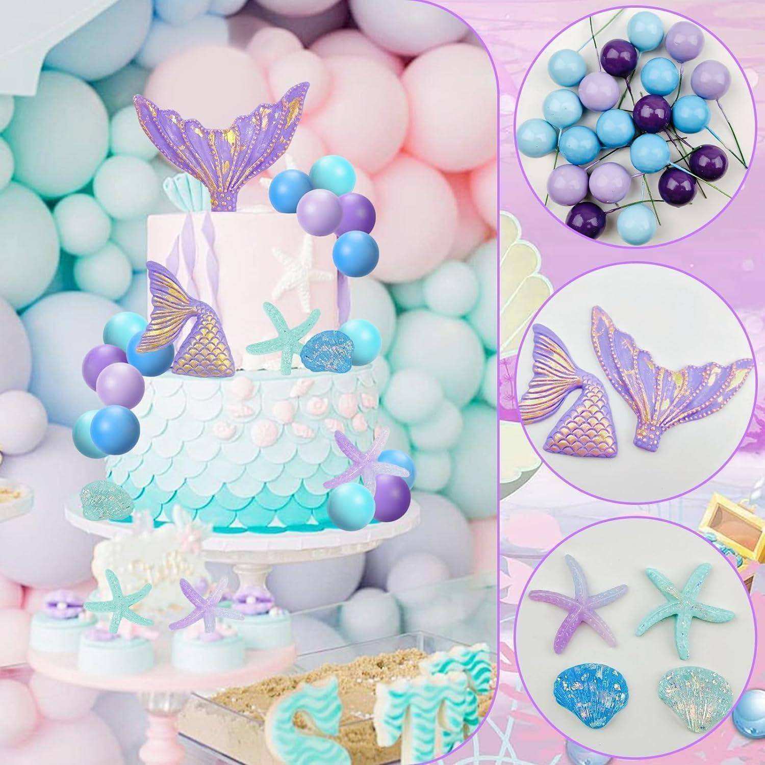 Eine pastellfarbene Geburtstagstorte mit Meerjungfrauenschwänzen, umgeben von hellblauen und rosa Luftballons. In der Nähe befinden sich Seesternkekse und maritime Dekorationen.