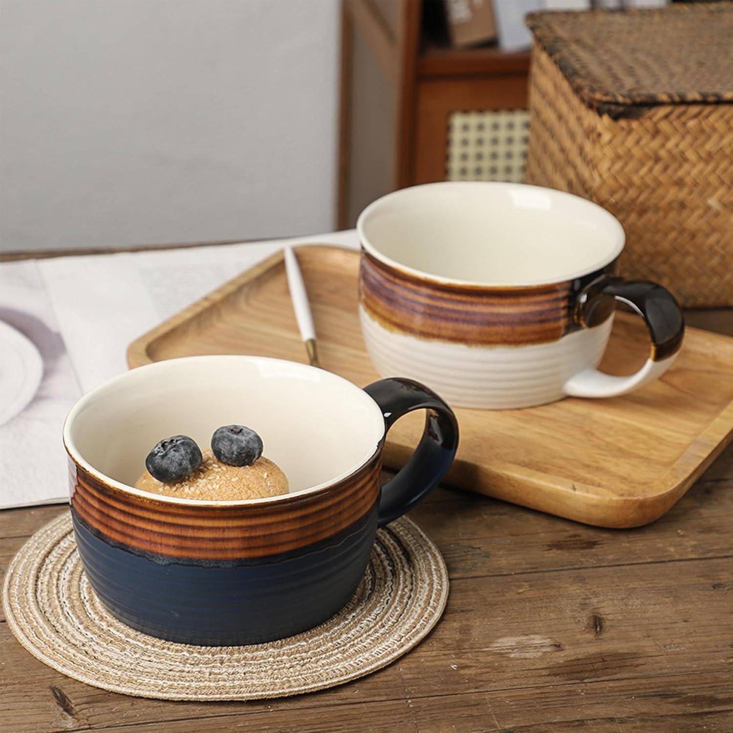 Zwei Keramikbecher mit braunen und blauen Streifen, die jeweils Joghurt mit Blaubeeren gefüllt sind, auf einem Holztisch mit einem Flechtkorb im Hintergrund.