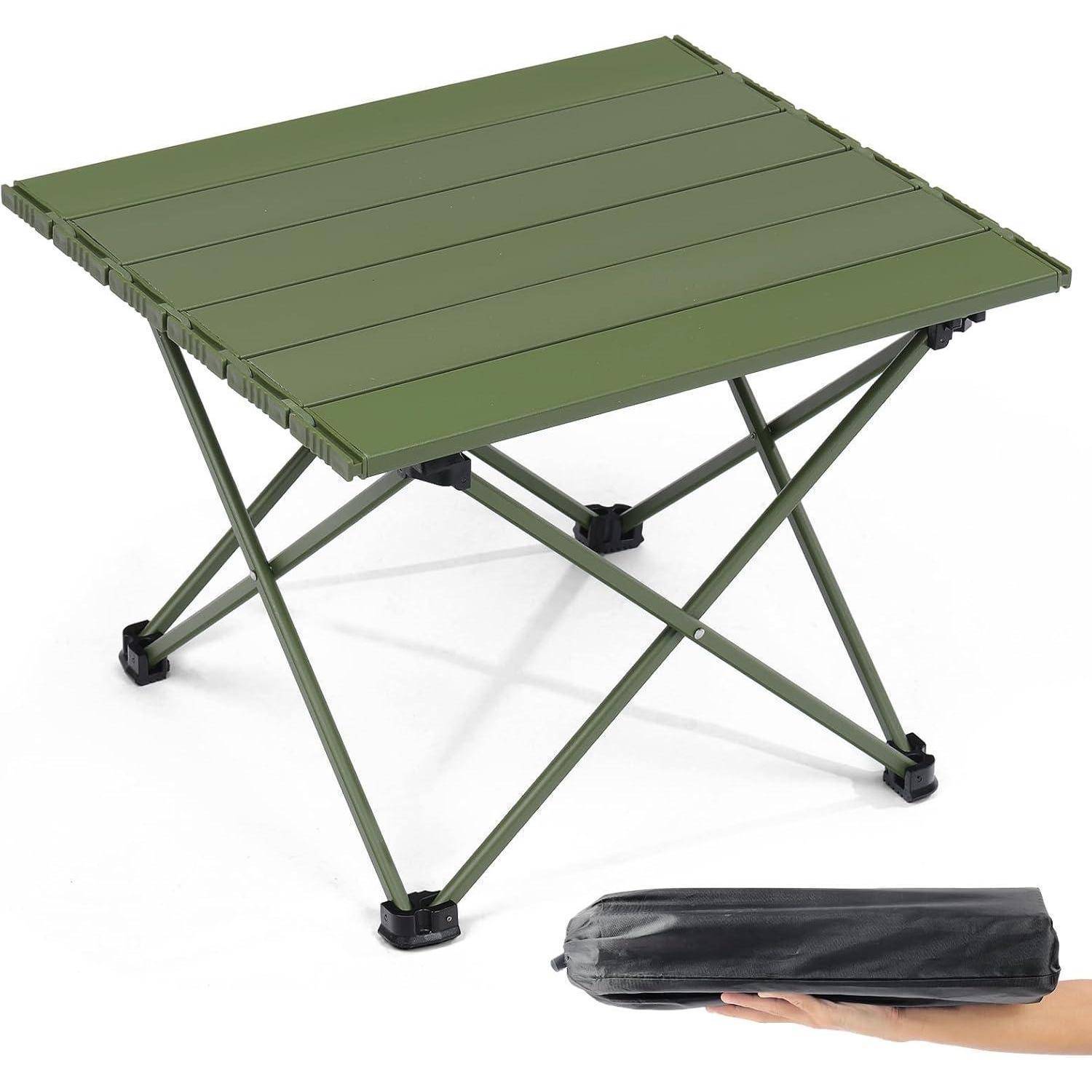 Ein zusammenklappbarer grüner Campingtisch mit einer Hand, die seine kompakte schwarze Tragetasche hält und die Transportfähigkeit des Tisches demonstriert.