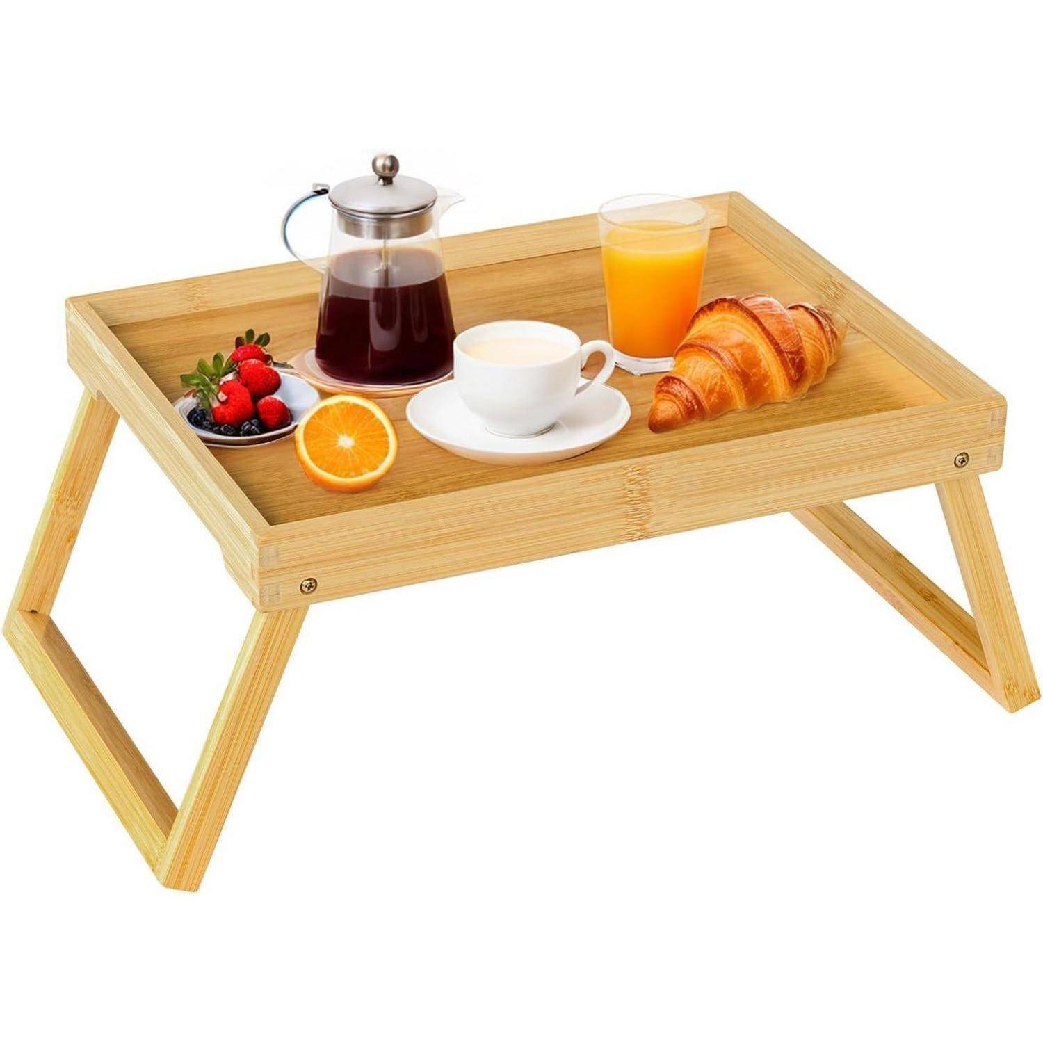 Ein Holztablett mit schrägen Beinen trägt eine Tasse Kaffee, Orangensaft, ein Croissant, frische Beeren, eine geschnittene Orange und einen kleinen Krug.