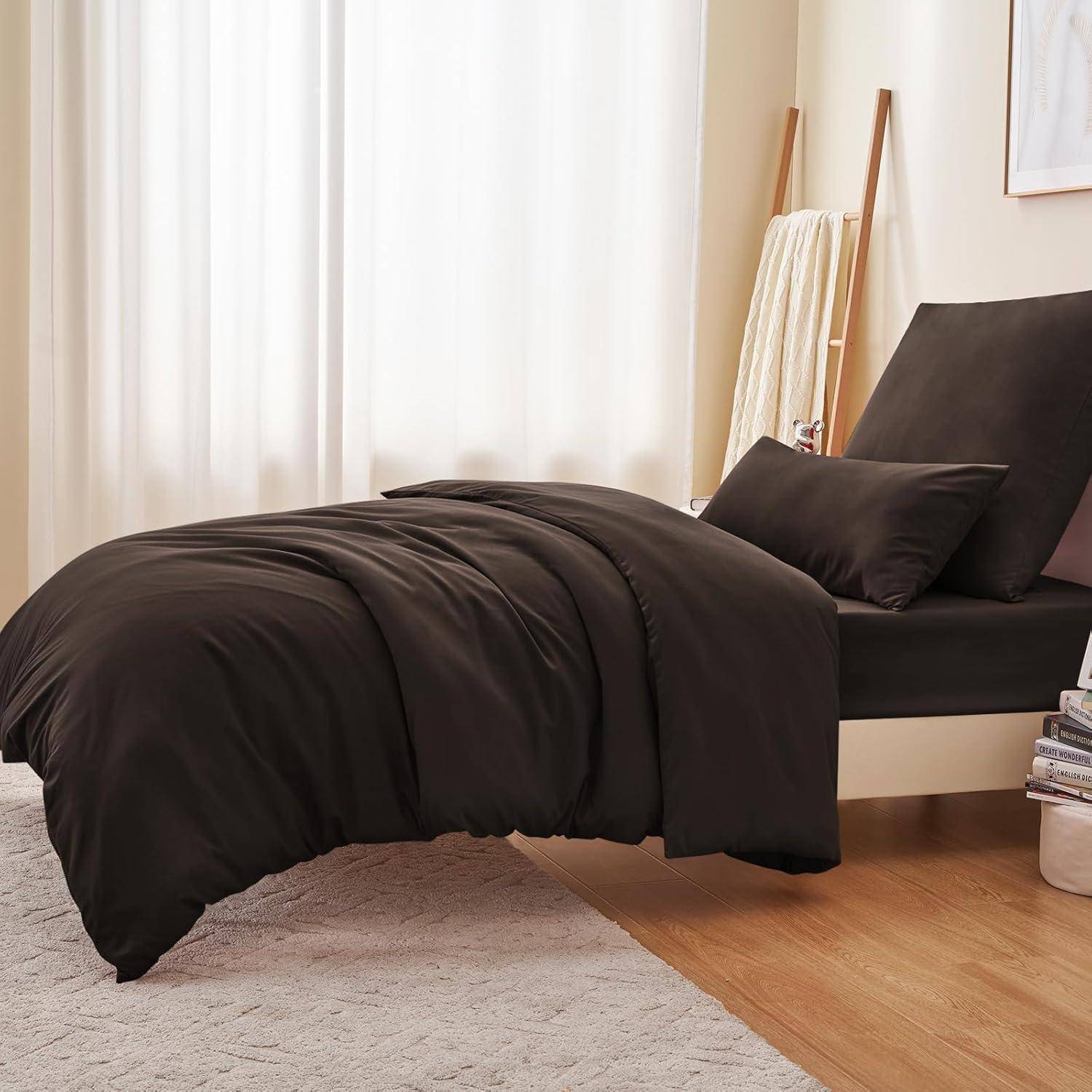 Ein ordentlich gemachtes Bett mit schwarzem Bettdecken und Kissen steht in einem warm beleuchteten Raum, mit einer zusammengelegten Decke und Lesebüchern in der Nähe.