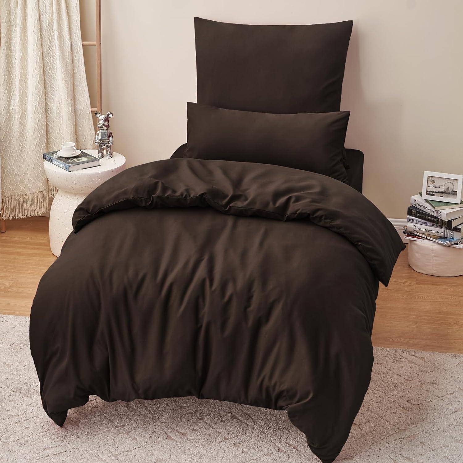 Ein Bett mit einem dunkelbraunen Bettüberwurf, Kissen und Zierkissen in einem gemütlichen Schlafzimmer mit einem hellbeigen Teppich und einem Beistelltisch, auf dem Bücher und Gläser stehen.