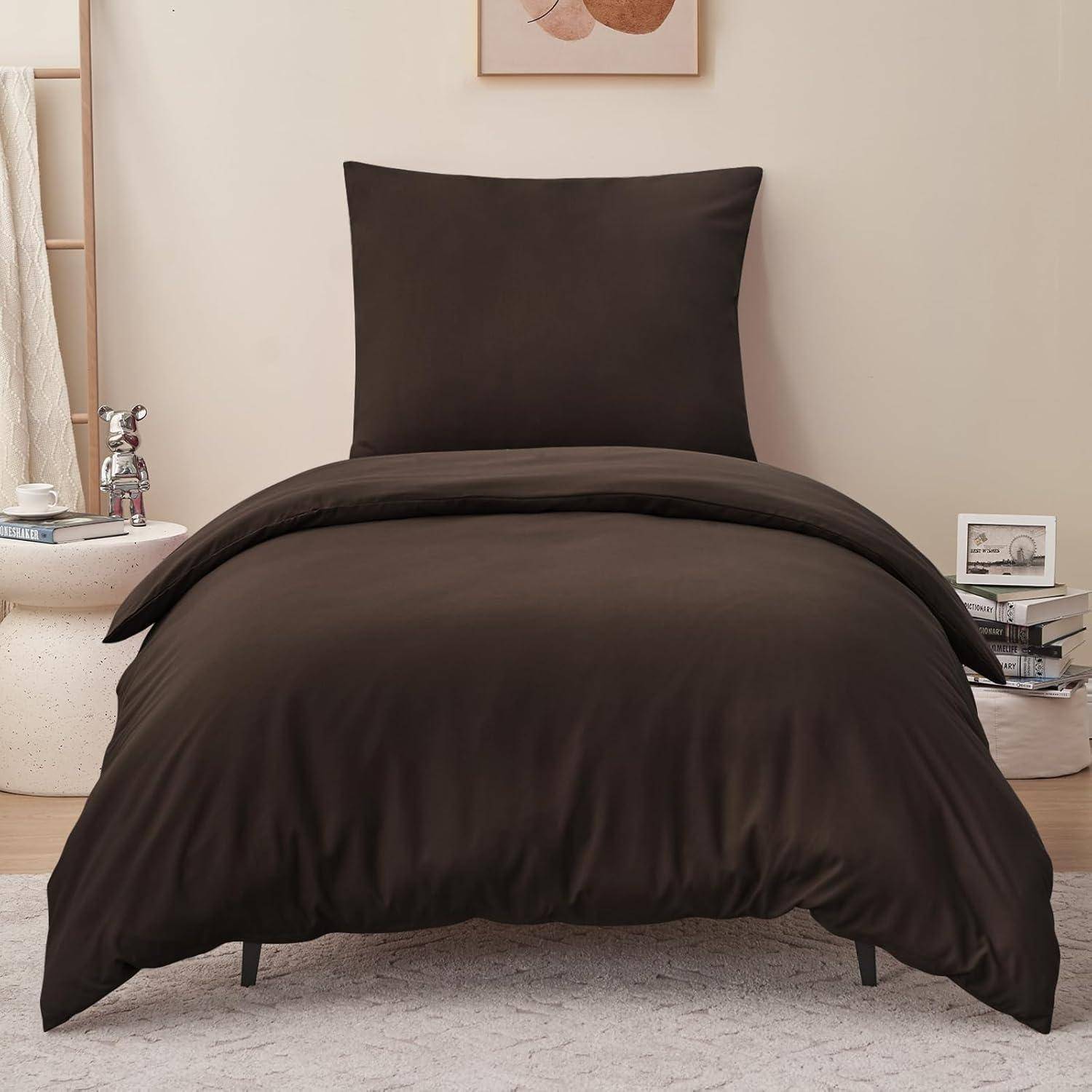 Ein ordentlich gemachtes Bett mit dunkelbrauner Bettwäsche, einem Kissen, einem Stapel Bücher daneben und einem kleinen Kunstwerk, das an der Wand darüber hängt.