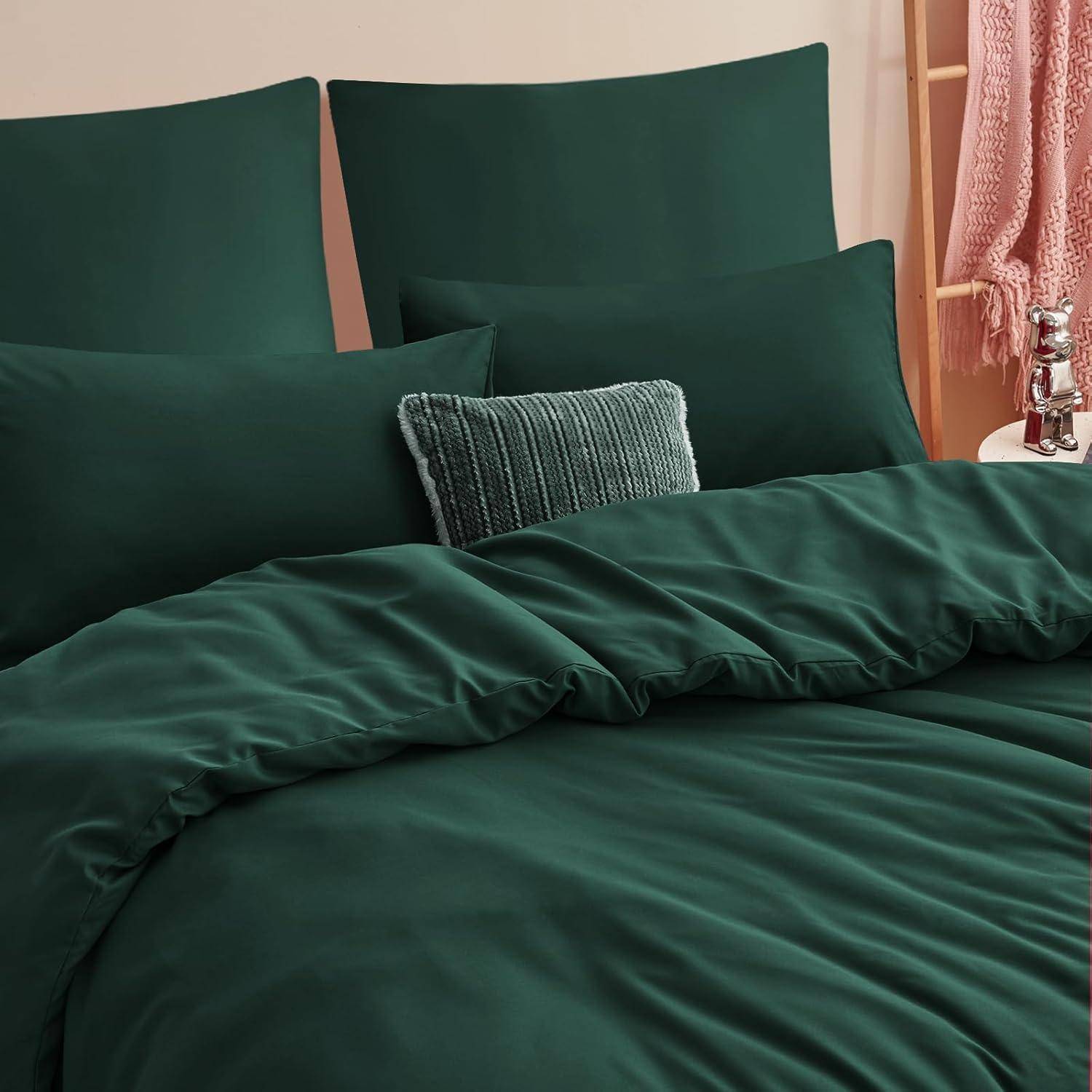Ein sauber gemachtes Bett mit dunkelgrüner Bettwäsche und einem strukturierten rechteckigen Kissen. Eine rosafarbene gewebte Decke ist in der Nähe an einer Holzleiter drapiert.