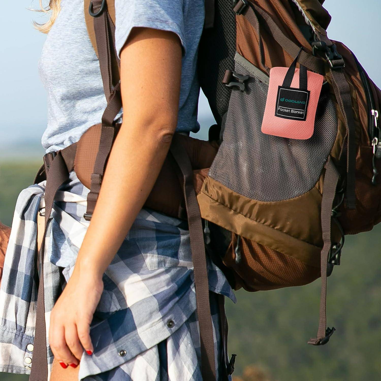 Eine Person steht im Freien mit einem Rucksack und einem Karohemd, das um die Taille gebunden ist, was auf eine Wanderungs- oder Naturaktivität hindeutet.