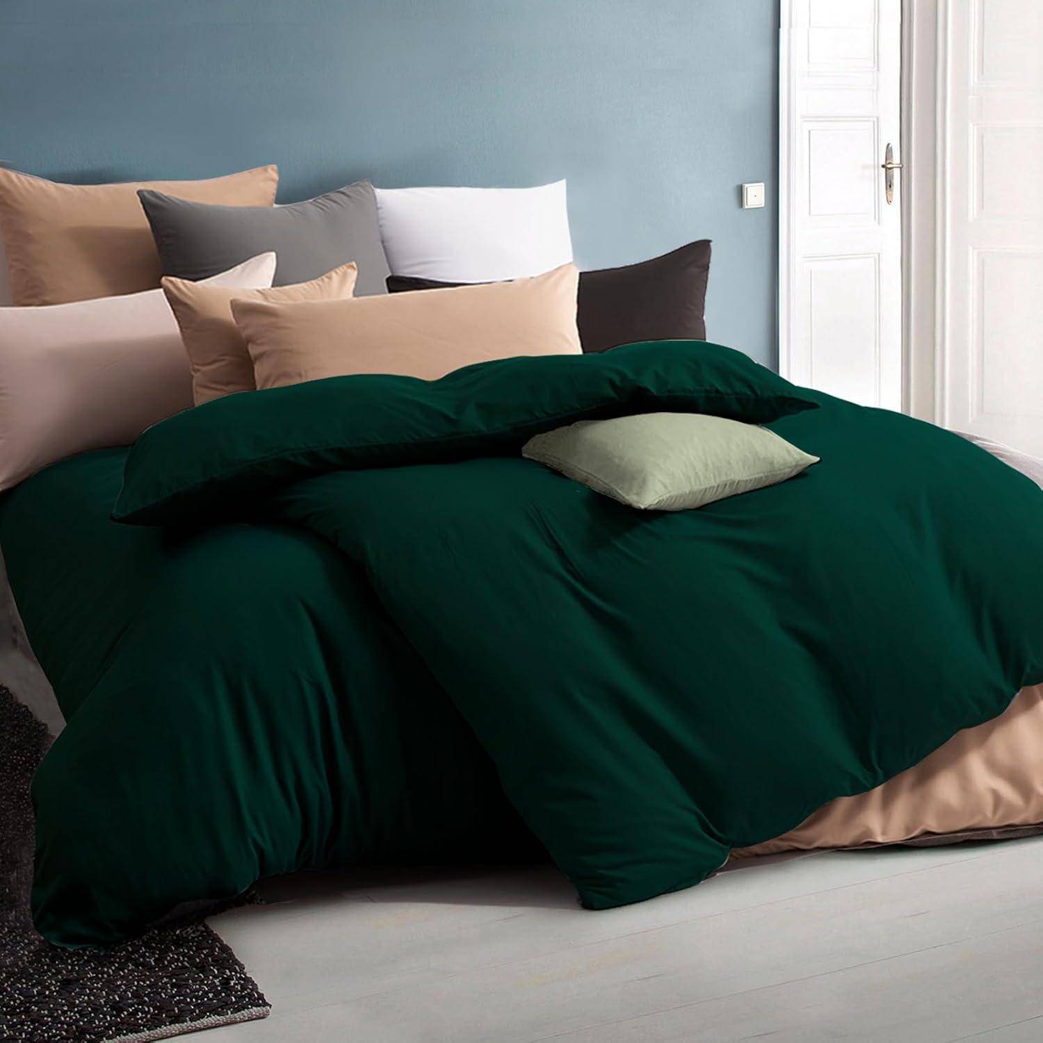 Ein ordentlich gemachtes Bett mit dunkelgrüner Bettwäsche und einer Vielzahl von bunt gemischten Kissen vor einer blassen Wand und einer angelehnte weißen Tür.