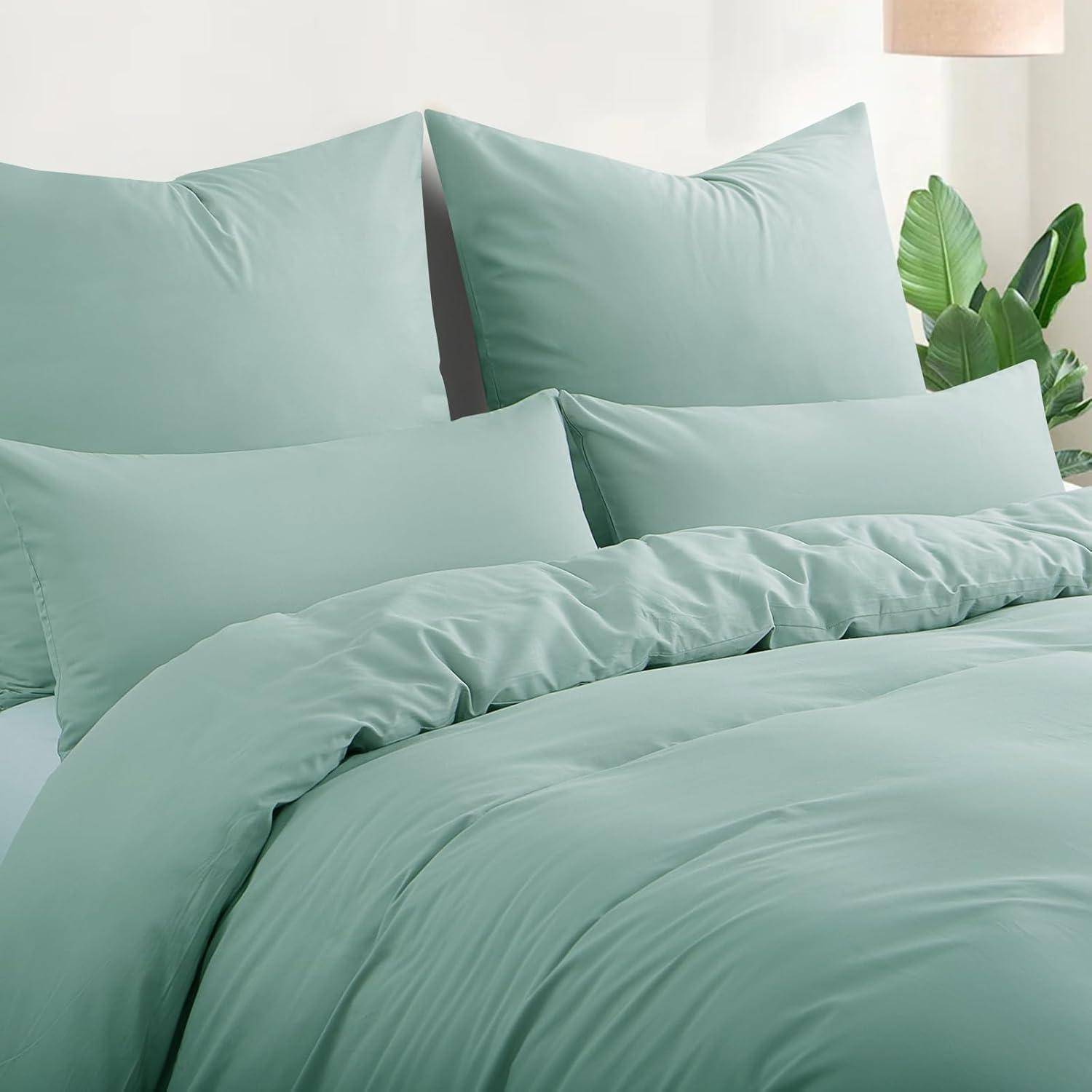 Ein ordentlich gemachtes Bett mit grüner Bettwäsche, einschließlich Kissen, Decke und Bettdecke. Eine Lampe und eine Pflanze befinden sich im Hintergrund.