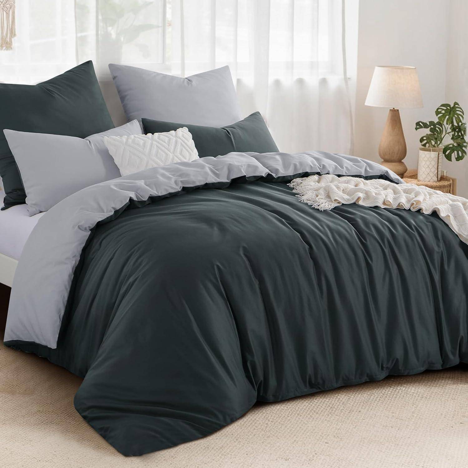 Ein ordentlich gemachtes Bett mit dunkelgrauer Bettwäsche, hell- und weißen Kissen, einer beigen Decke, einer Holzlampe und einer Topfpflanze auf dem Nachttisch.