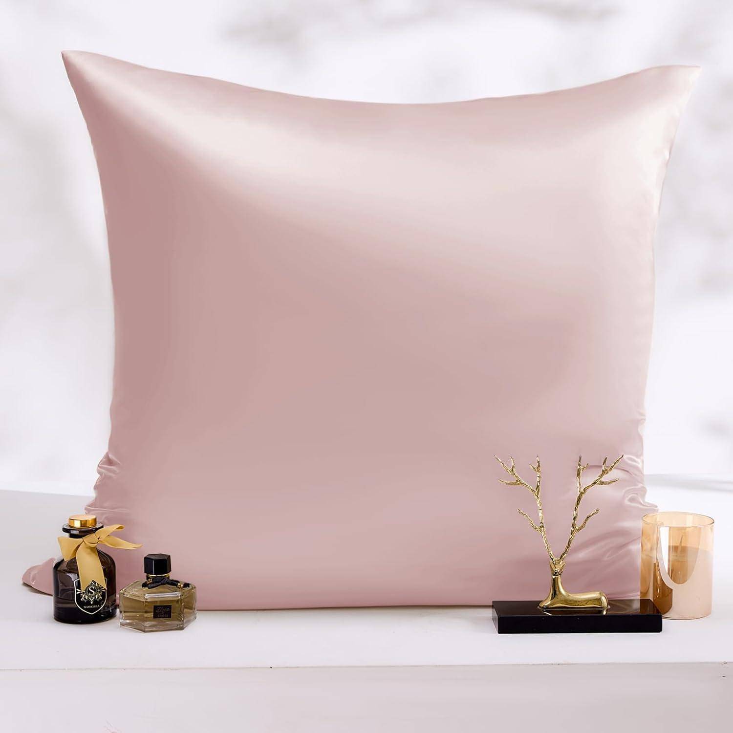 Ein glänzendes Satin-Kissen ist mittig platziert, flankiert von zwei Parfümflakons und einem kleinen dekorativen goldenen Mini-Baum auf einer weißen Oberfläche.