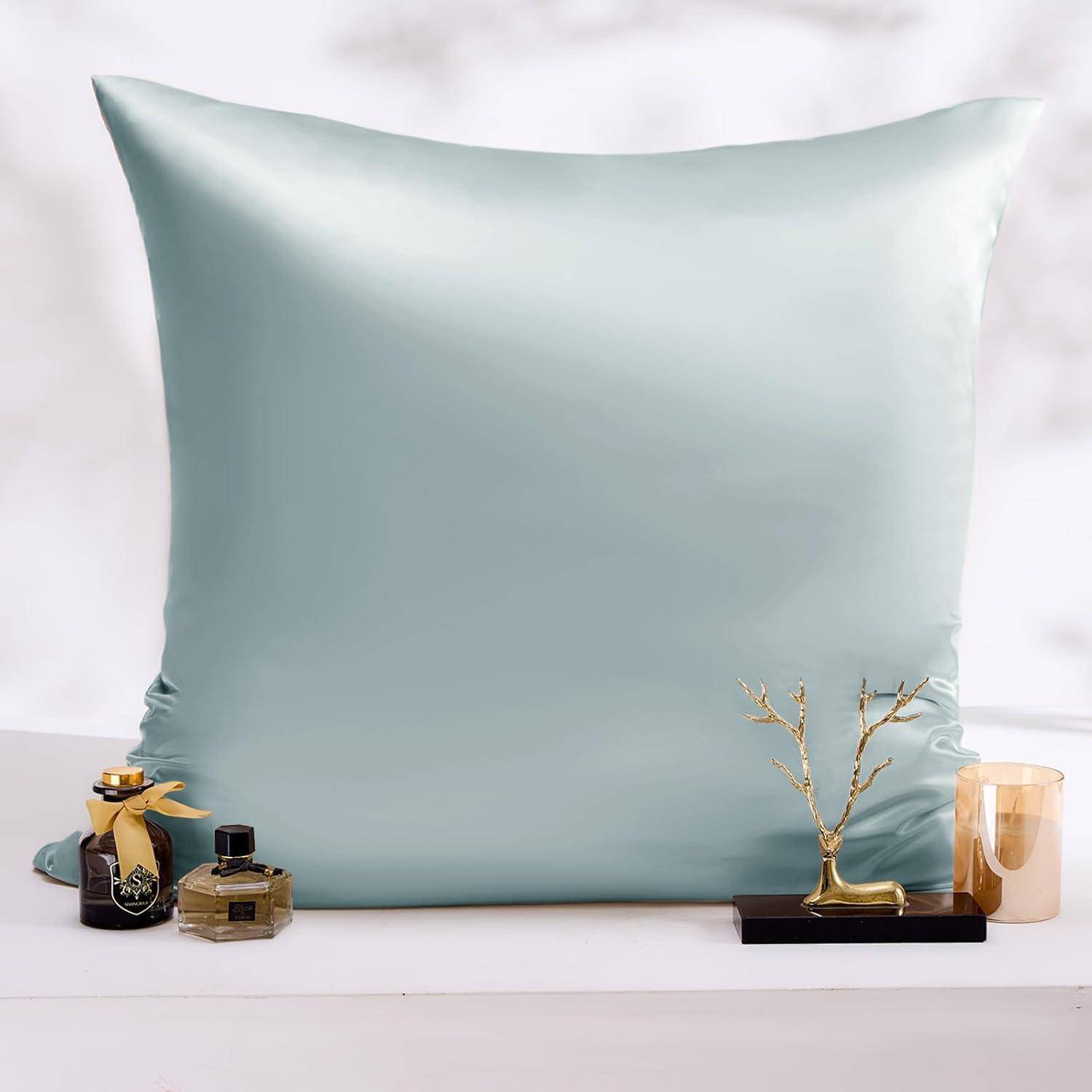 Ein hellblauer Satin-Kissenbezug wird zusammen mit Parfümflakons und einem kleinen Dekorationsobjekt im Vordergrund präsentiert.