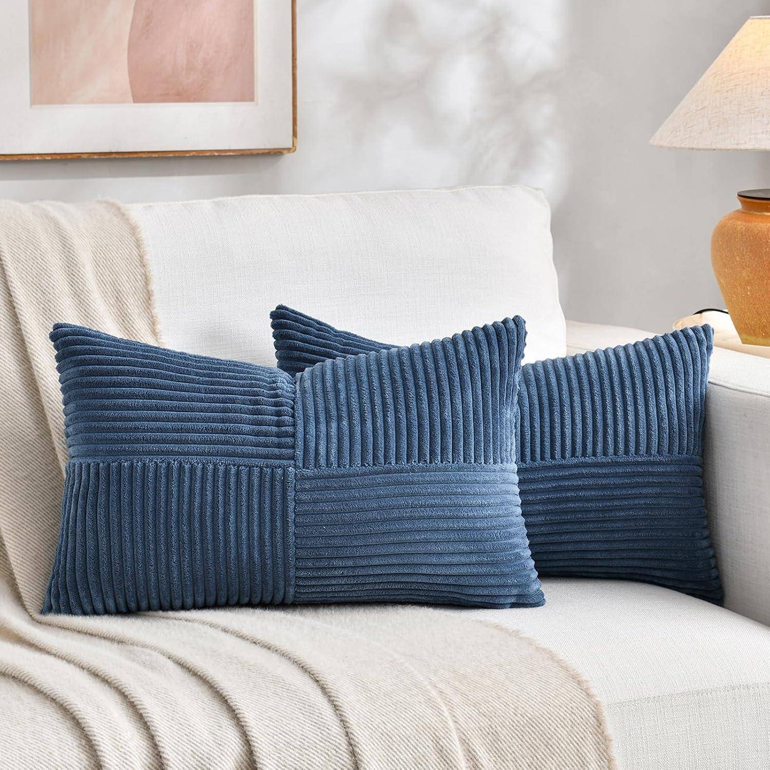 Zwei blaue gerippte Kissen auf einem weißen Sofa mit einer beigen Decke, neben einer Tischlampe, in einer gemütlichen Wohnzimmeratmosphäre.