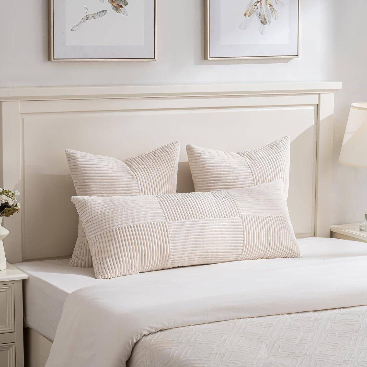 Ein Bett mit beige gestreiften Kissen und einer weißen Bettdecke in einem gemütlichen Schlafzimmer, mit gerahmten Kunstwerken an der Wand und einem Nachttisch mit einer Lampe.