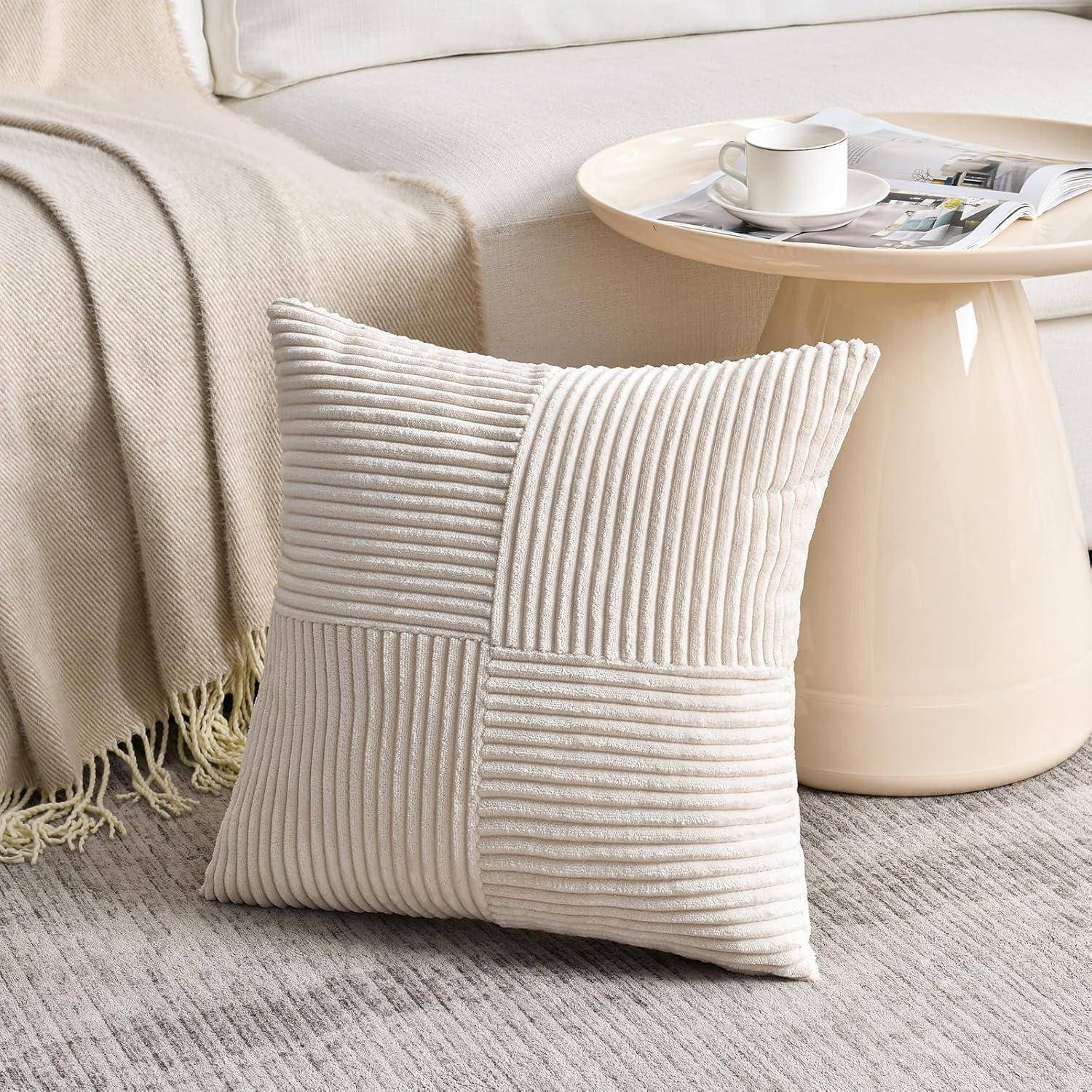 Ein beiger Cordkissen liegt auf einem teppichbelegten Boden, an einer hellgefärbten Couch gelehnt. Ein runder Couchtisch mit einer Tasse und einer Zeitschrift befindet sich in der Nähe.