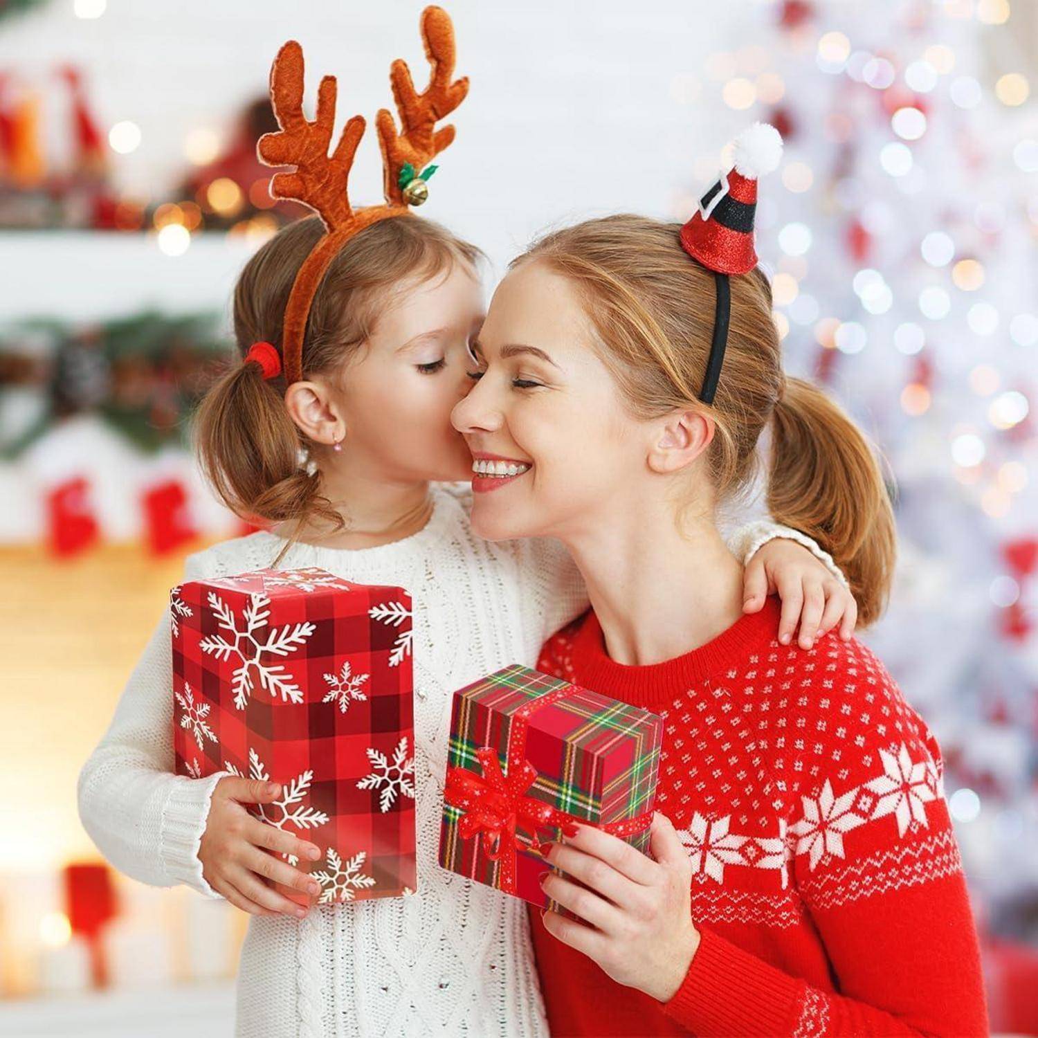 Ein Kind mit Rentiergeweih und eine Frau mit einem Weihnachtsmann-Haarreif, beide lächelnd und Geschenke in Geschenkpapier haltend, in einer festlichen Atmosphäre.