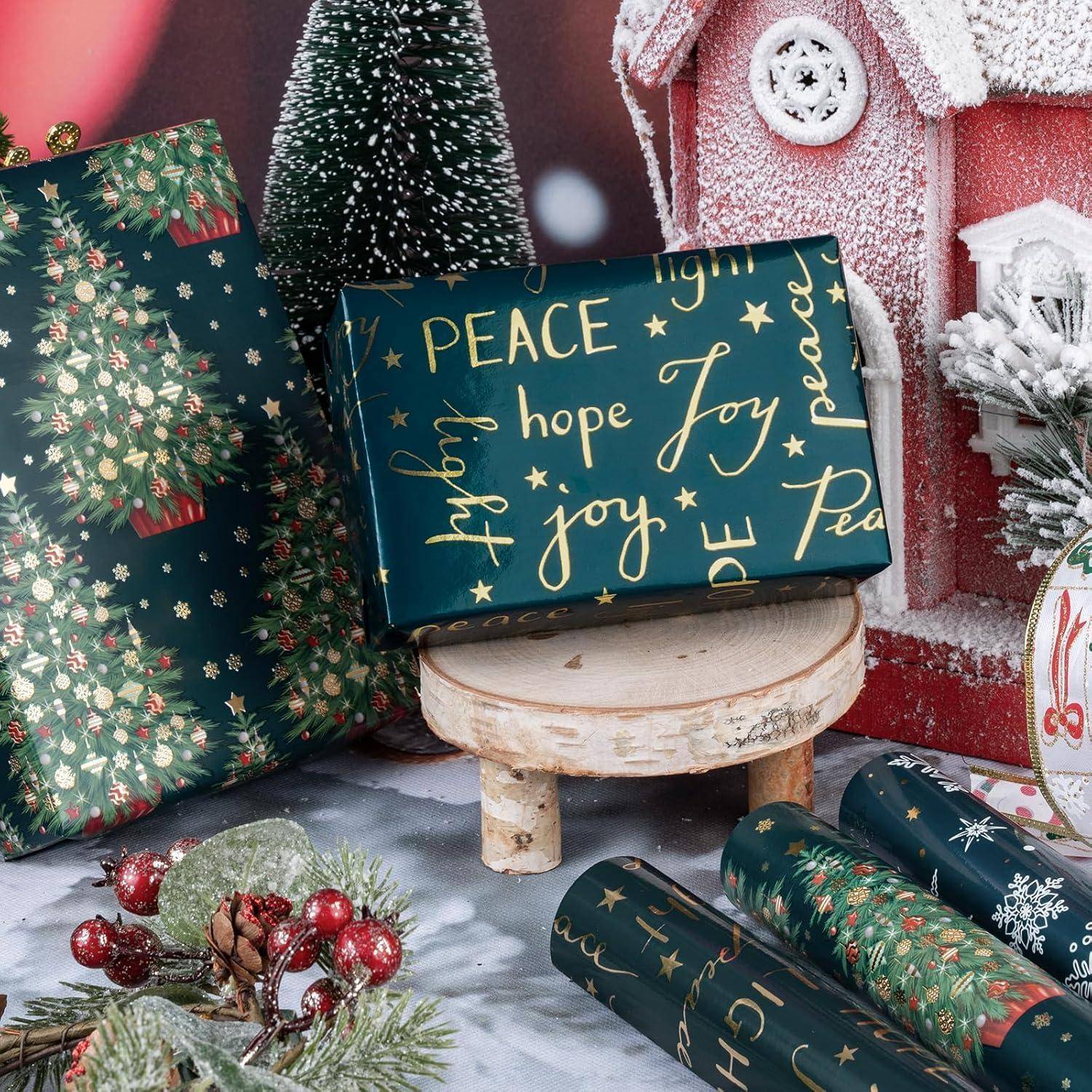 Weihnachtlich gestaltete Geschenke, eingepackt in festliches Papier mit 'FRIEDEN' und 'Freude' Schriftzügen, umgeben von Weihnachtsdekoration wie einem kleinen Weihnachtsmannhaus und Tannenzweigen.