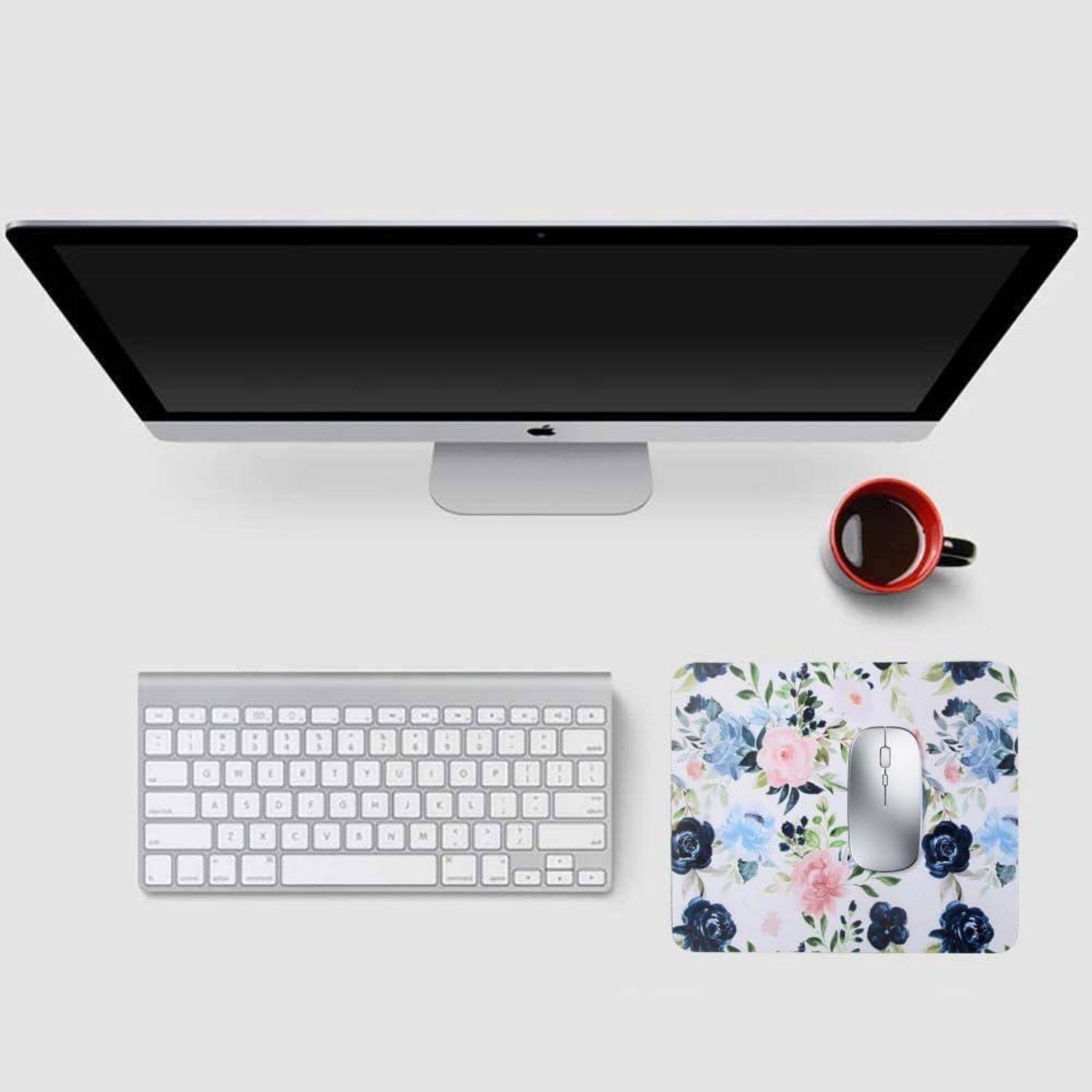 Ein Computermonitor, eine Tastatur und ein blumiges Mauspad mit einer Maus sind auf einem Schreibtisch angeordnet. Eine rote Kaffeetasse steht neben dem Monitor.