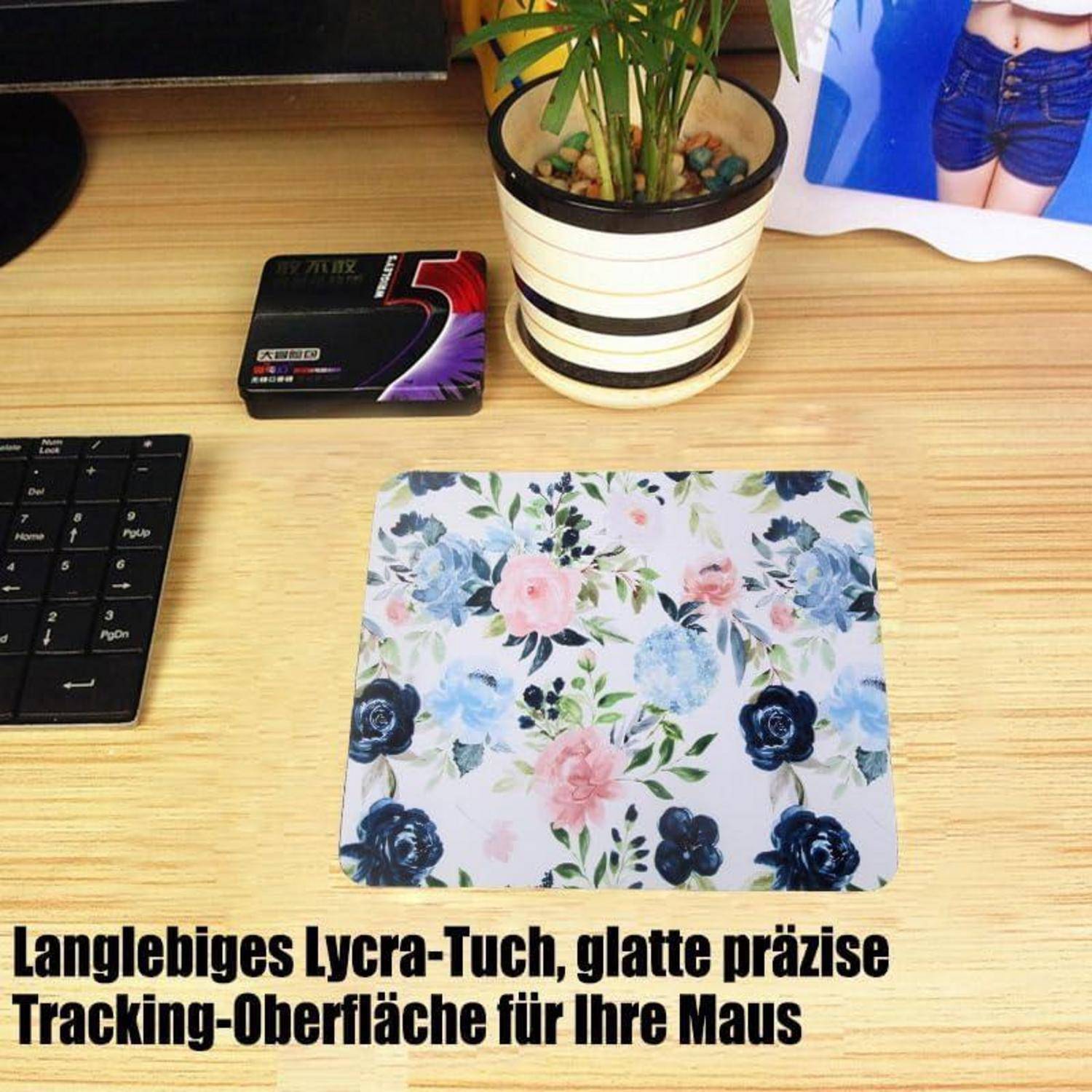 Blumen-Mousepad auf Schreibtisch mit mehrfarbigem Blumenmuster und schwarzer Tastatur daneben. Text unten: 'Langlebiges Lycra-Tuch, glatte präzise Tracking-Oberfläche für Ihre Maus'. Ein kleiner Pflanzenübertopf ist oben abgebildet.