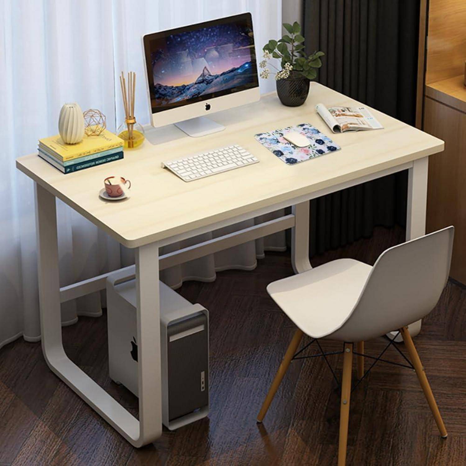 Ein aufgeräumter Schreibtisch in einem modernen Büroraum mit einem Computer, der eine Naturwallpaper zeigt, einer Tastatur, Büchern, einer Pflanze und einem Blumen-Mousepad.