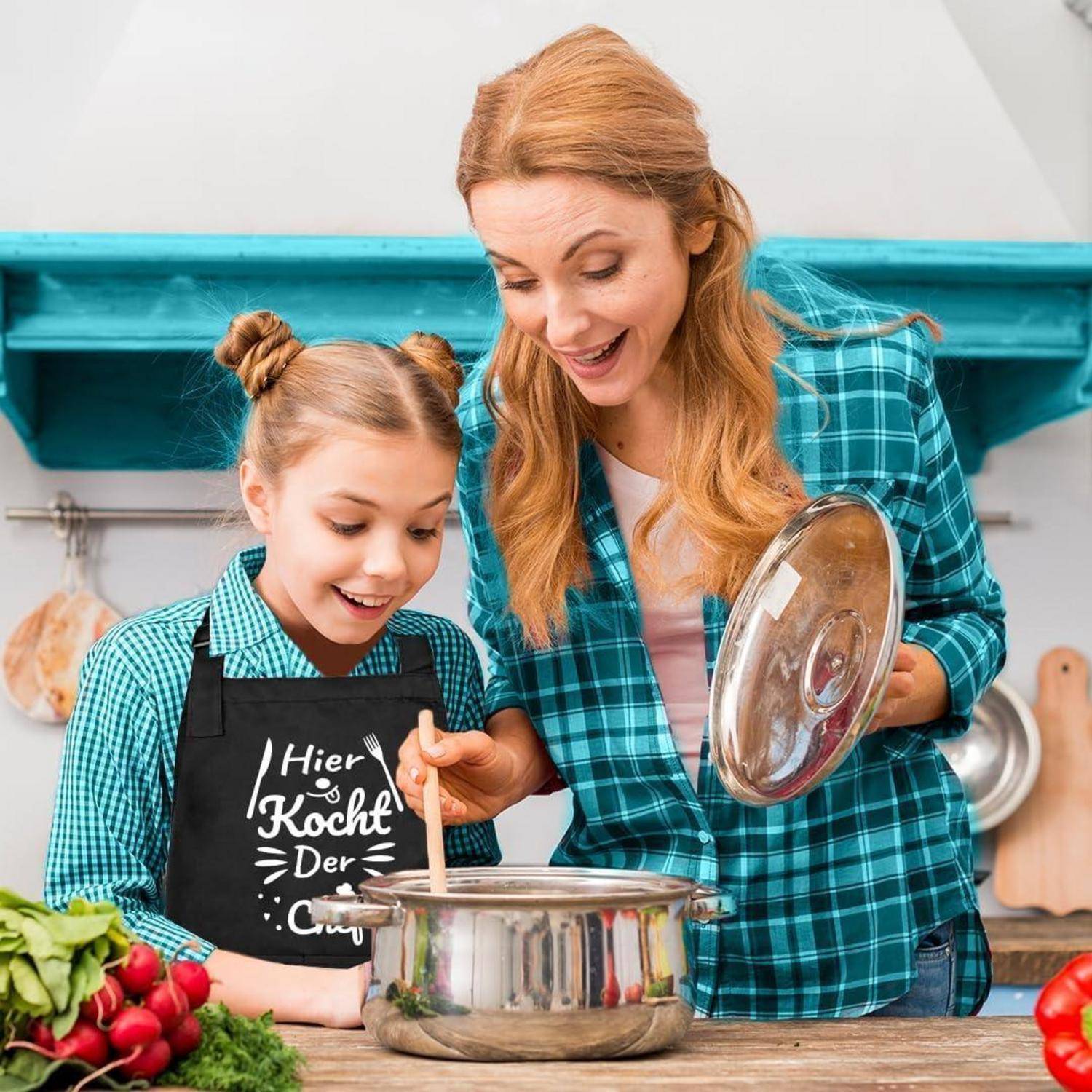 Mutter und Tochter kochen gemeinsam in einer Küche, beide lächeln auf den Topf auf dem Herd. Gemüse liegt auf der Anrichte.