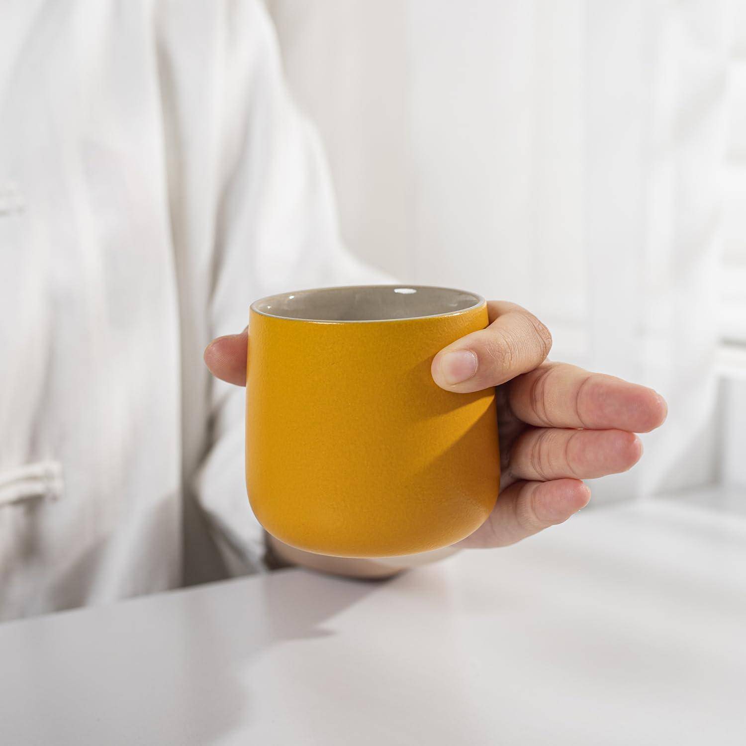Eine Person in einem weißen Gewand, die eine gelbe Tasse hält, was eine entspannte Morgensituation oder eine Teezeit andeutet.