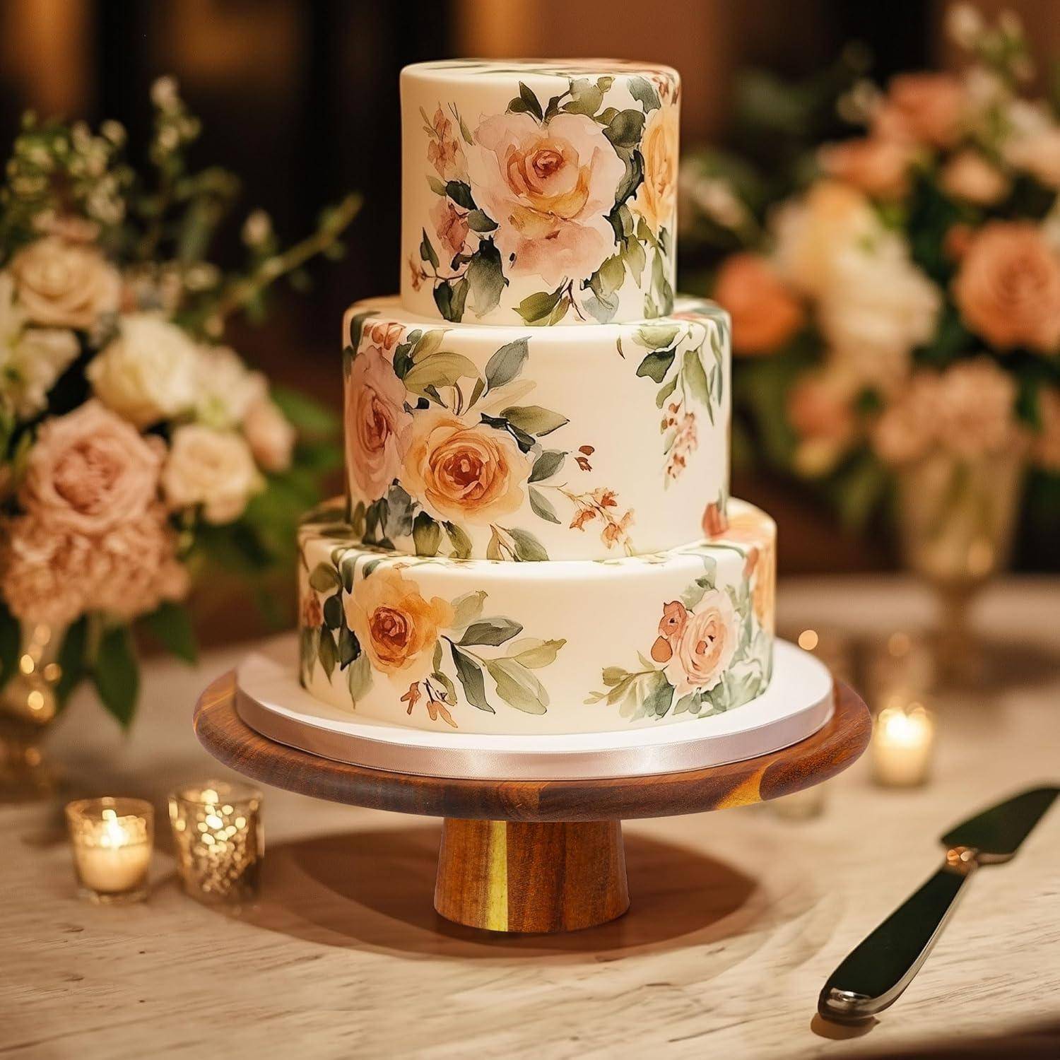 Eine dreistöckige Torte, verziert mit Pfirsich- und Rosafarben-Blumendesigns, präsentiert auf einem Holzständer, umgeben von Blumenarrangements und brennenden Kerzen.
