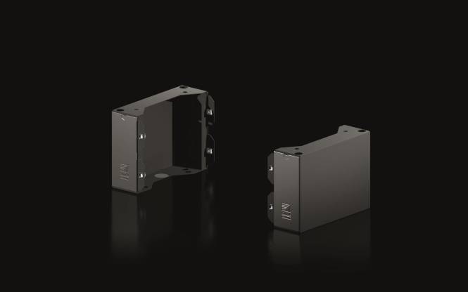 Zwei schwarze Metallgehäuse mit abgeschrägten Seiten und Befestigungslöchern, die auf einer glänzenden Oberfläche stehen.
