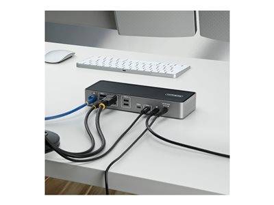 Eine Dockingstation, die mit mehreren Kabeln und Geräten verbunden ist, steht auf einem weißen Schreibtisch. Eine Tastatur und eine Maus sind ebenfalls zu sehen.