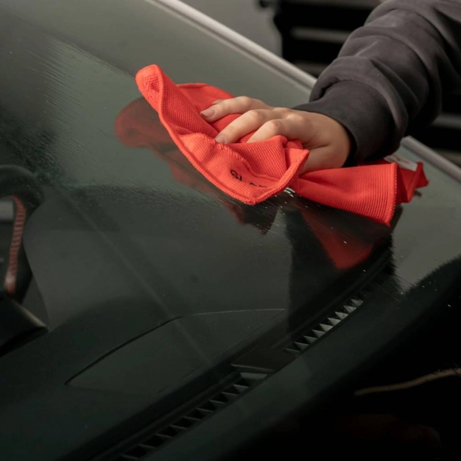 Eine Person benutzt ein orangefarbenes Tuch, um die Innenseite der Windschutzscheibe eines Autos zu reinigen und konzentriert sich darauf, Verschmutzungen wegzuwischen, um eine klare Sicht zu gewährleisten.